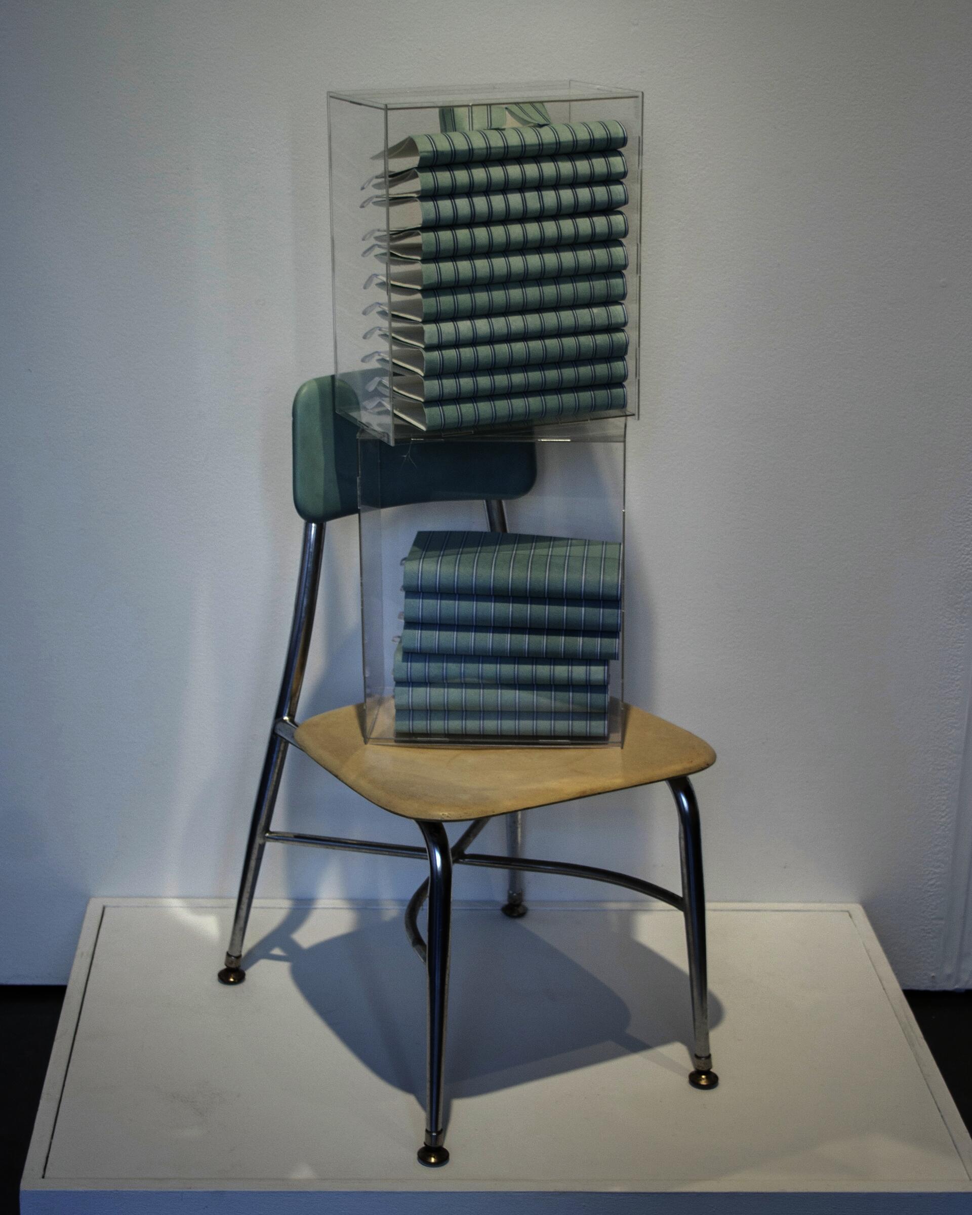 Three-layer photopolymer letterpress on kozo paper, folded and stacked in acrylic boxes to mimic folded shirts, placed on top of a found wooden chair.