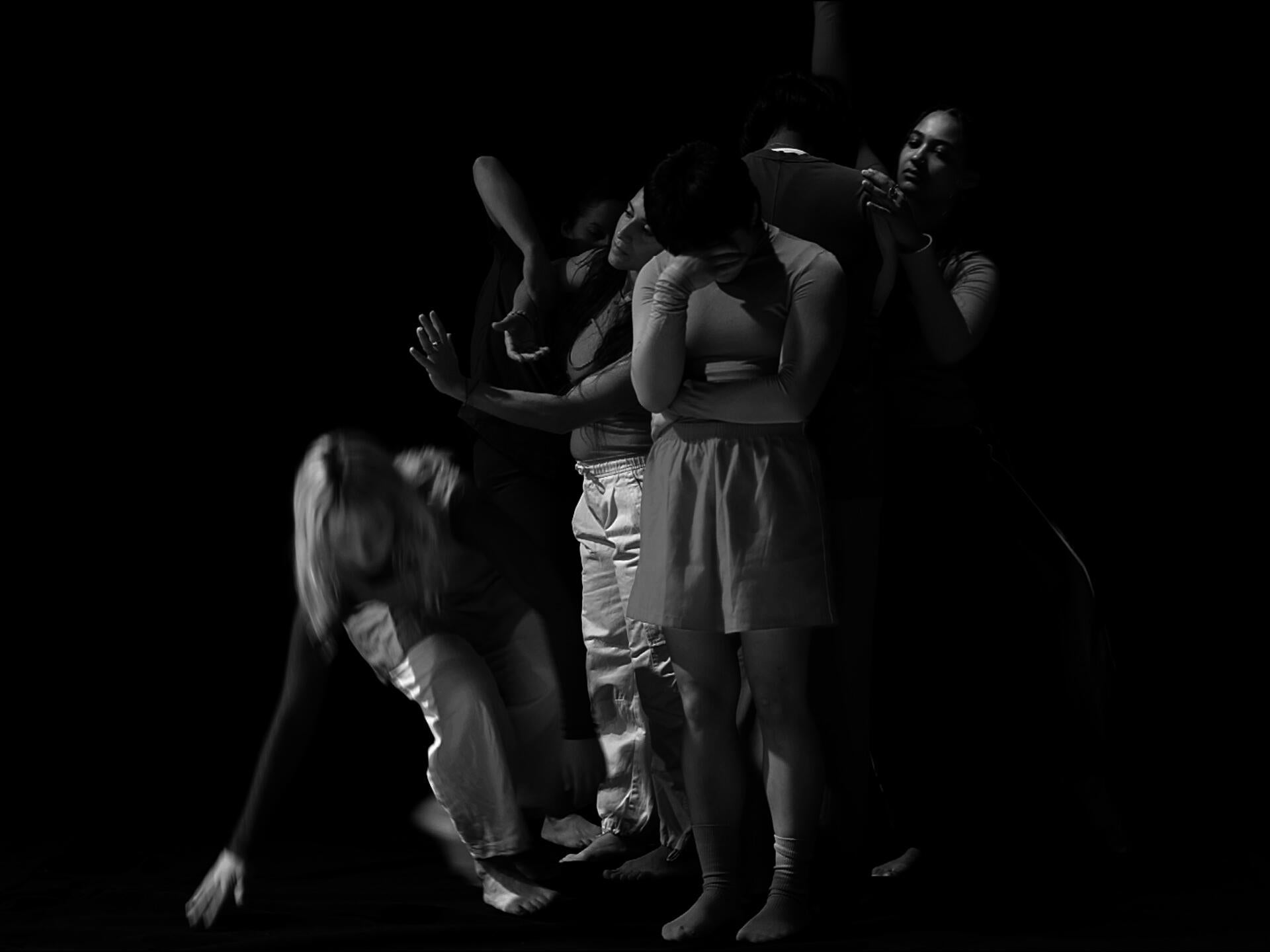 Six female and non-binary identifying dancers create various shapes with their bodies against a black background in this black and white video still.