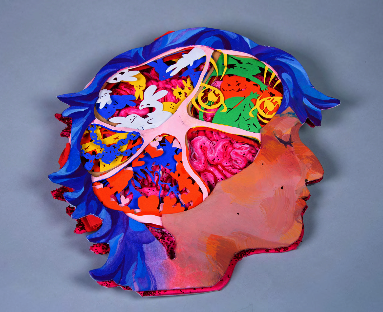 Tunnel book made with, museum board, paper, gouache, acrylic, air dry clay, glitter, glue and gloss finish. Book shaped of a face side profile, where the brain should be is an opening with 5 sections. 1 of a brain, one of bunny like creatures, one with memories locked away and one of love. 