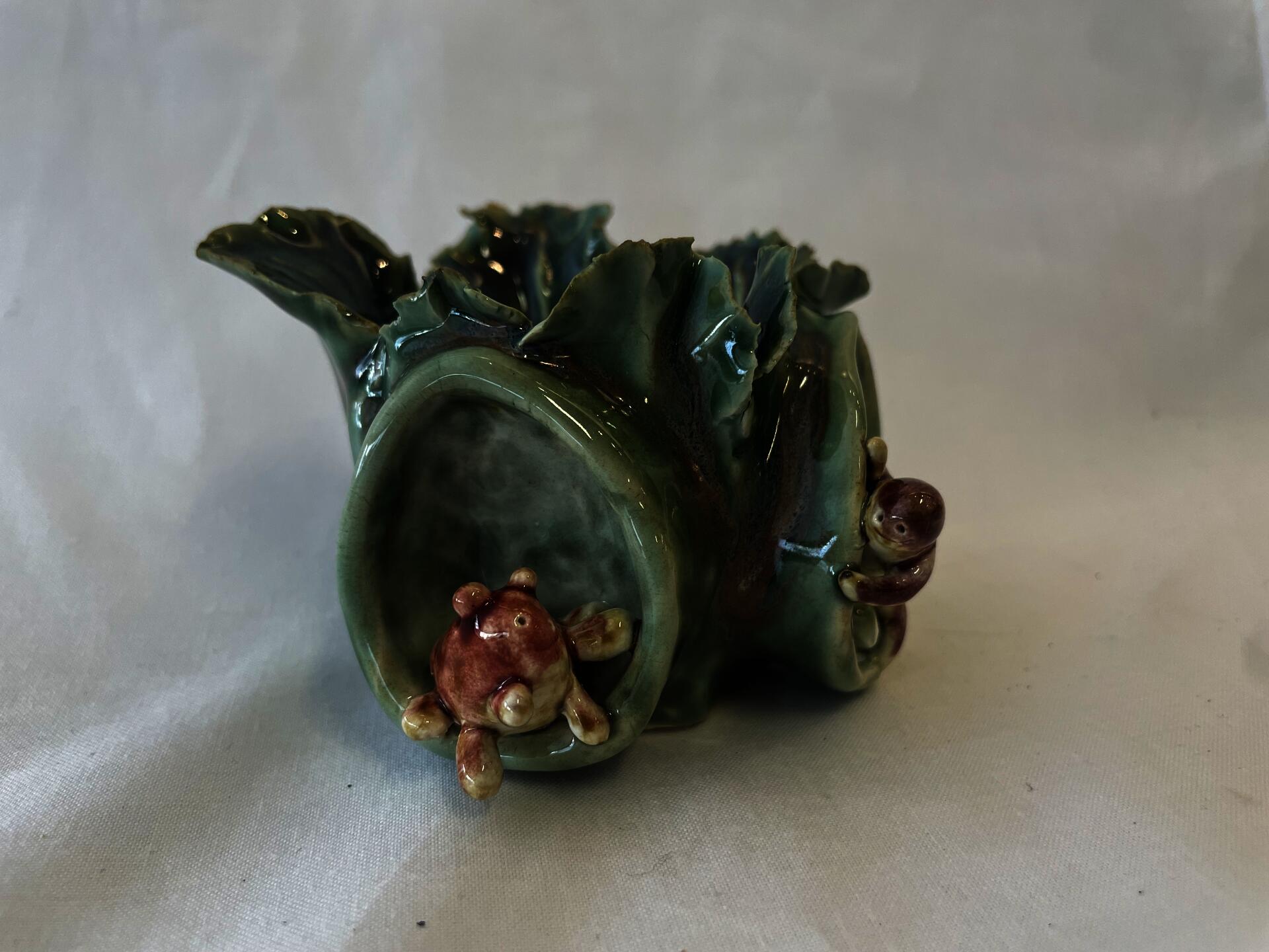 Ceramic bowel made using pinching clay techniques to have a lettuce like appearance, two hand sculpted creatures are on the outside in their own built in holes on the outside of the bowl. Both creatures are peaking around the corner to say hi to each other. Creatures are glazed orange and brown, lettuce bowl is green.