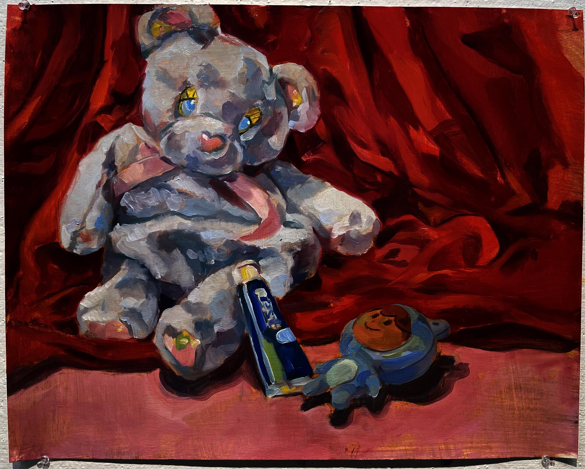 Still life with red fabric background and blue color objects in front consisting of a toy bear, blue stuffie and toothpaste bottle. Oil paint on gessoed canvas.