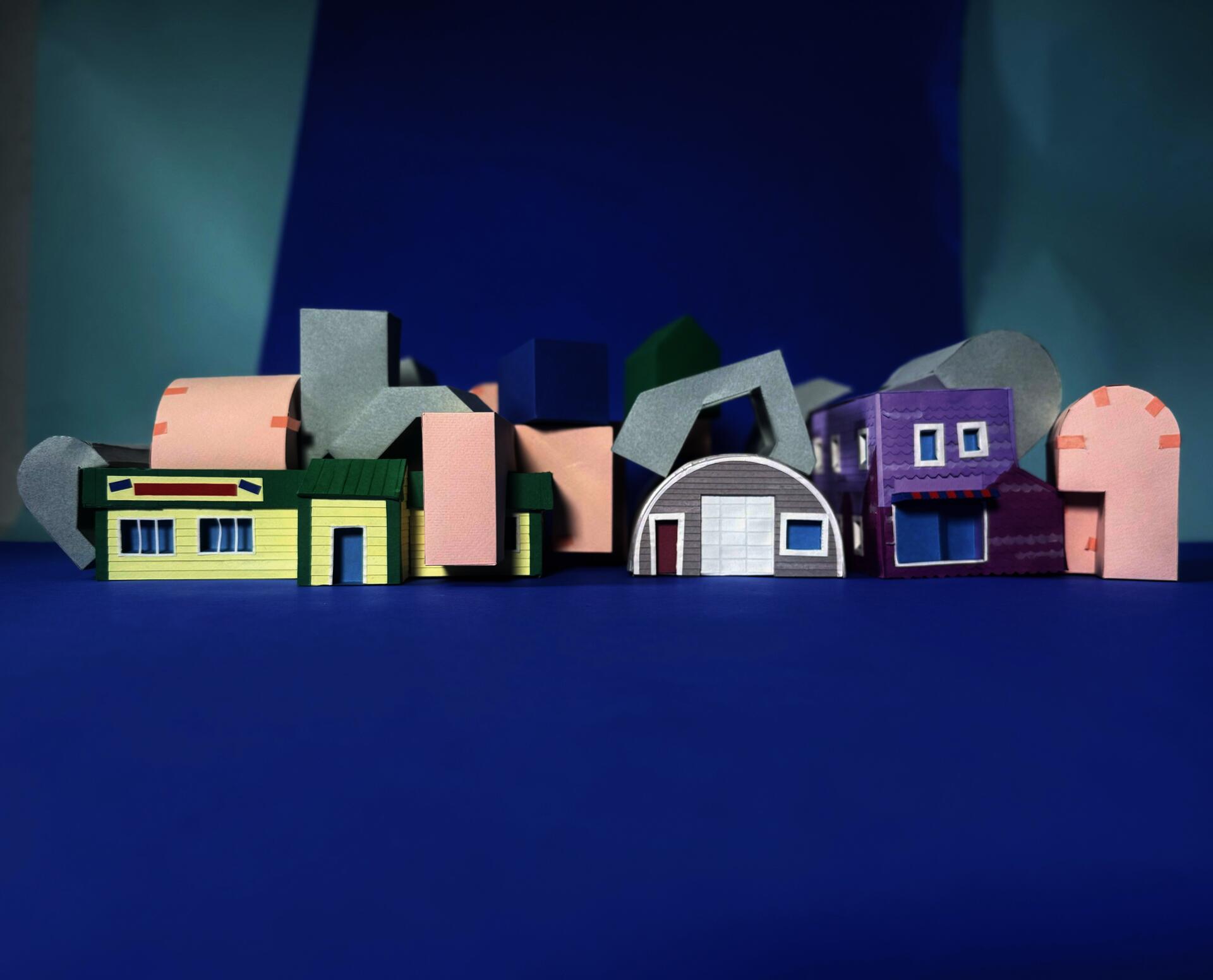 several paper models of building massing and existing buildings sit on a blue background. 