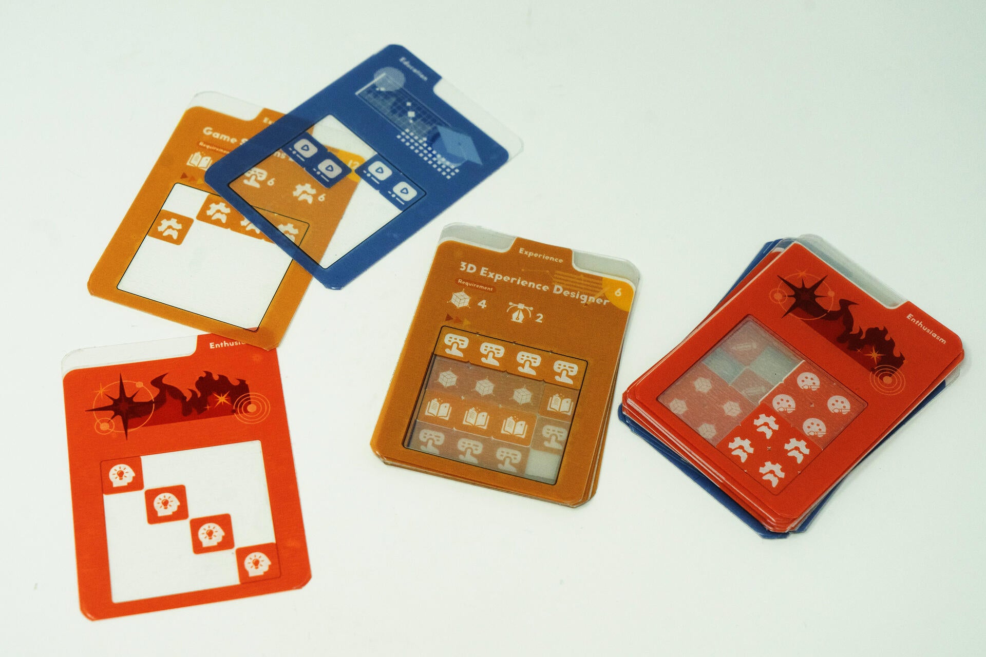 Transparent acrylic overlay cards layered over colorful role cards in a tabletop board game prototype about resume-building and persuasive communication.