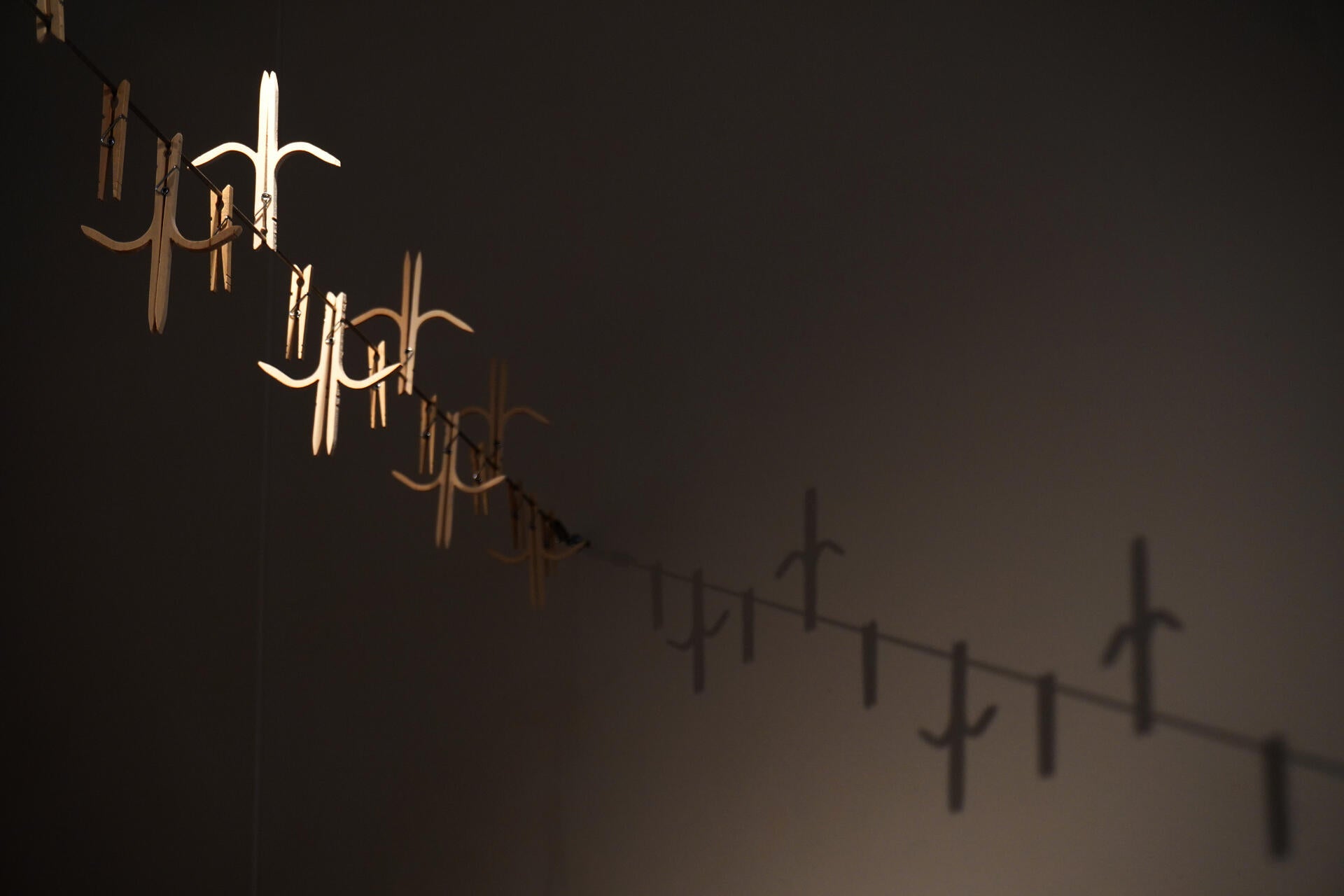 Modified wooden clothespins on a steel clothesline that have a shape of an anticlimbing fence with spikes pointing upwards and downwards.