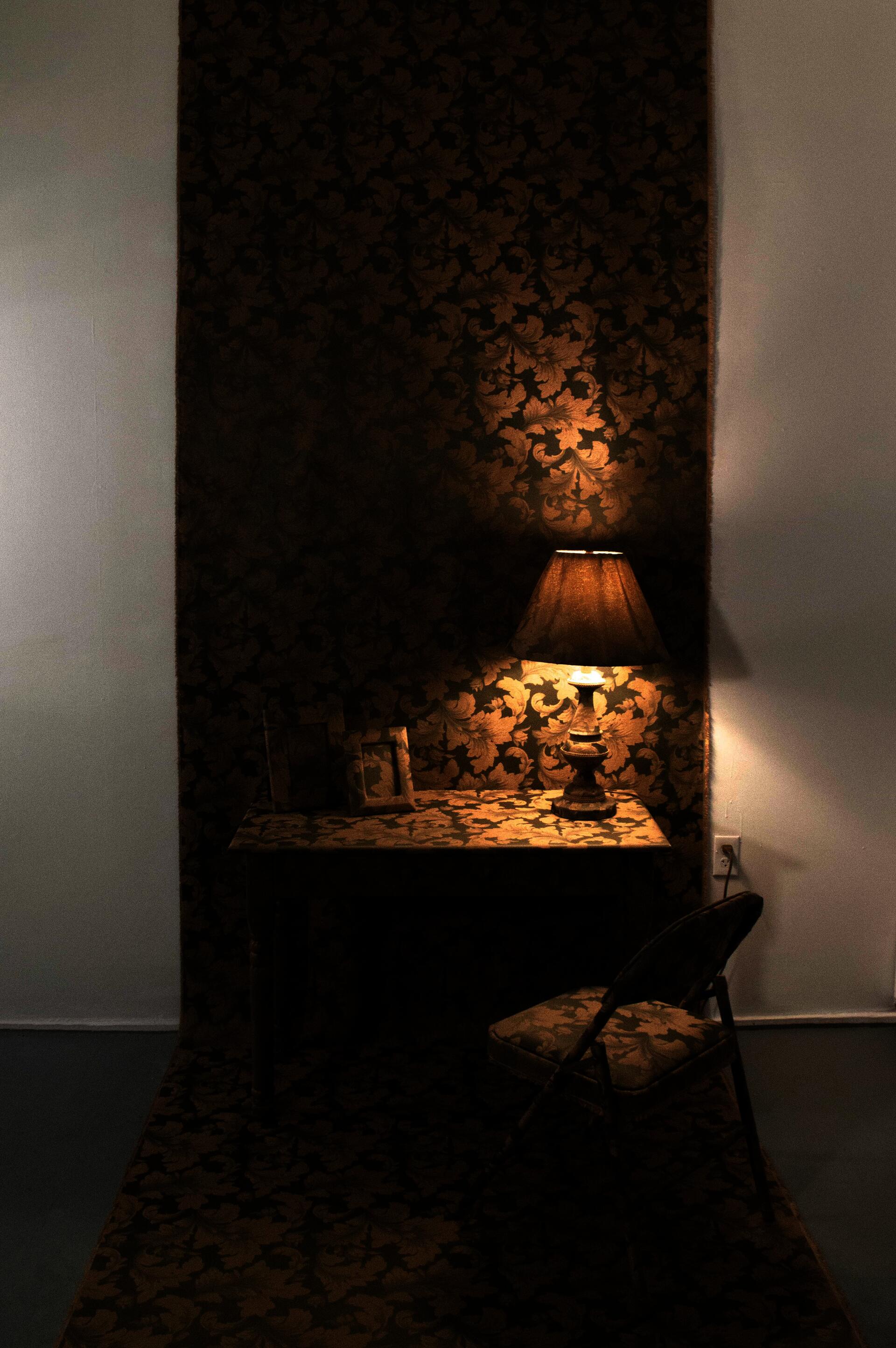 A table, a chair, two photo frames, and a lamp covered with a golden and olive green flower pattern upholstery fabric.