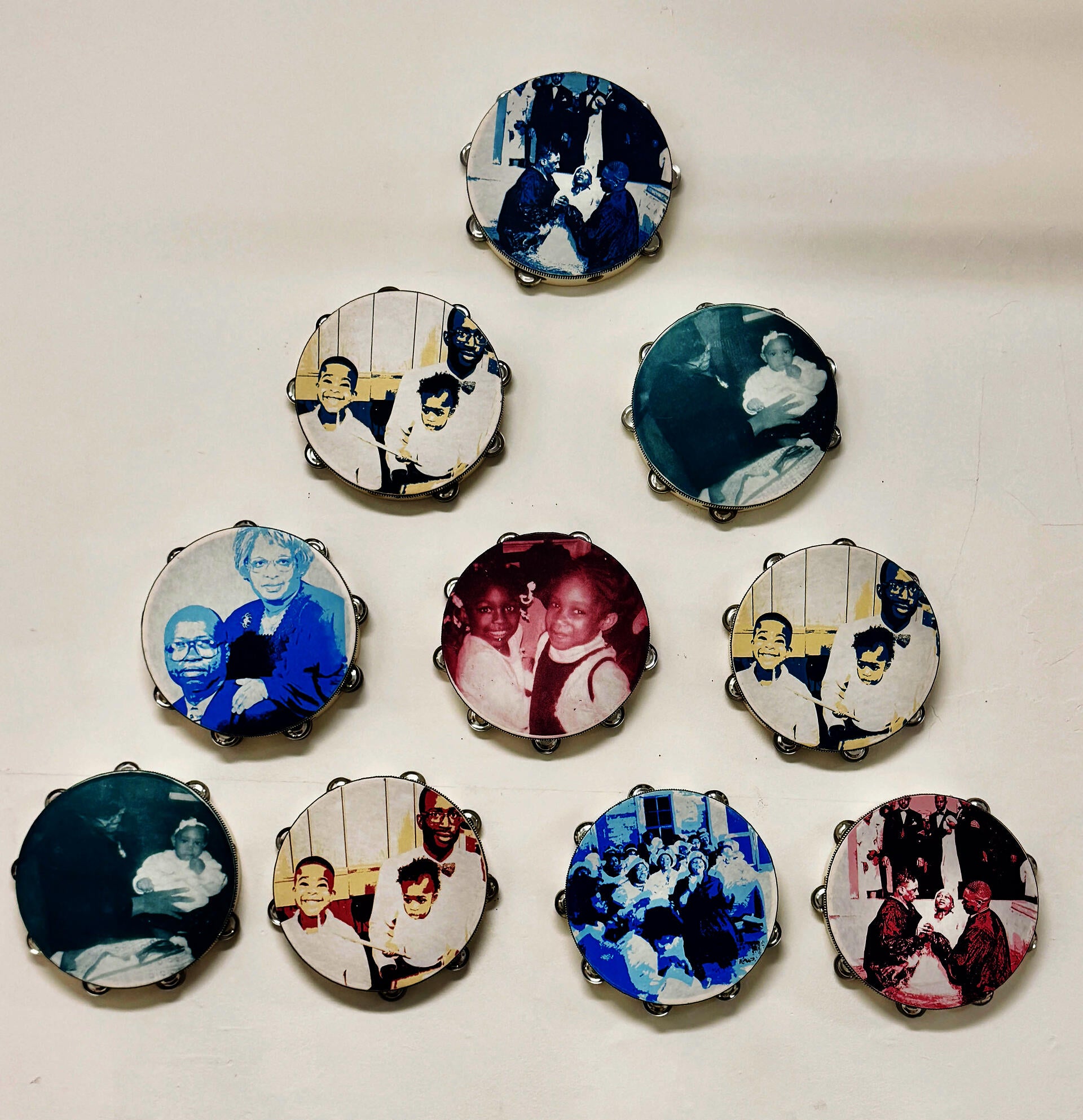 Triangular pyramid of ten wooden tambourines. The faces on the tambourine show magenta, cyan, yellow, and deep purple. Screen-printed portraits of the artist’s family and traditions that occur in a church setting, such as baptisms, praise, and worship.