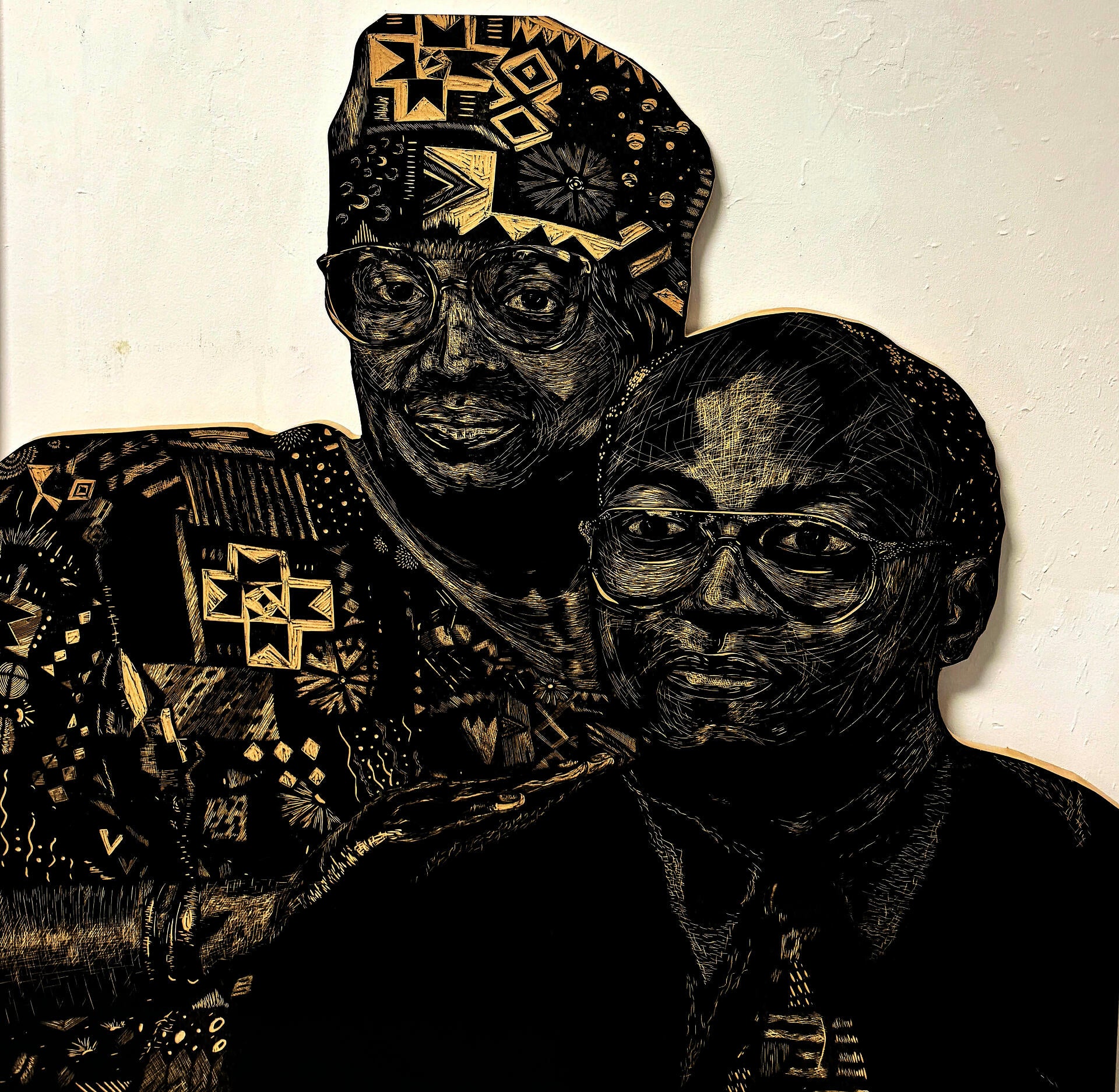 A large-scale woodcut in black and white. Portrait of the artist’s grandparents, Arthur and Cynthia Adams. Cynthia stands behind Arthur, hands on his shoulder. Cynthia wears patterned African fabric, and Arthur wears a black shirt with a patterned tie. 