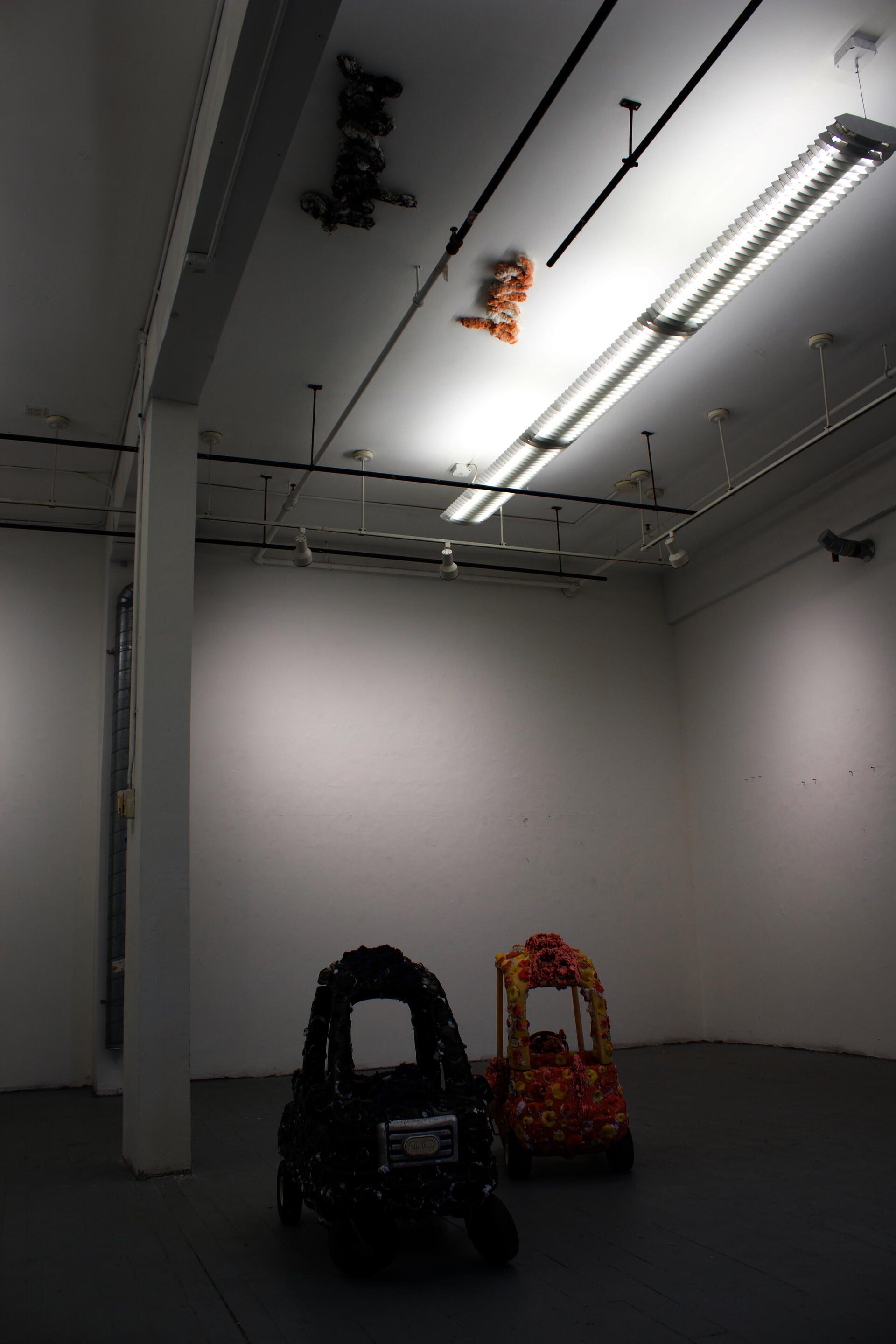 Establishing shot of 2 ride on cars, one black and one orange and yellow. They look spotted because of extensive hole saw openings, which were then stuffed with stuffed animal stuffing and re-capped with a melted hole