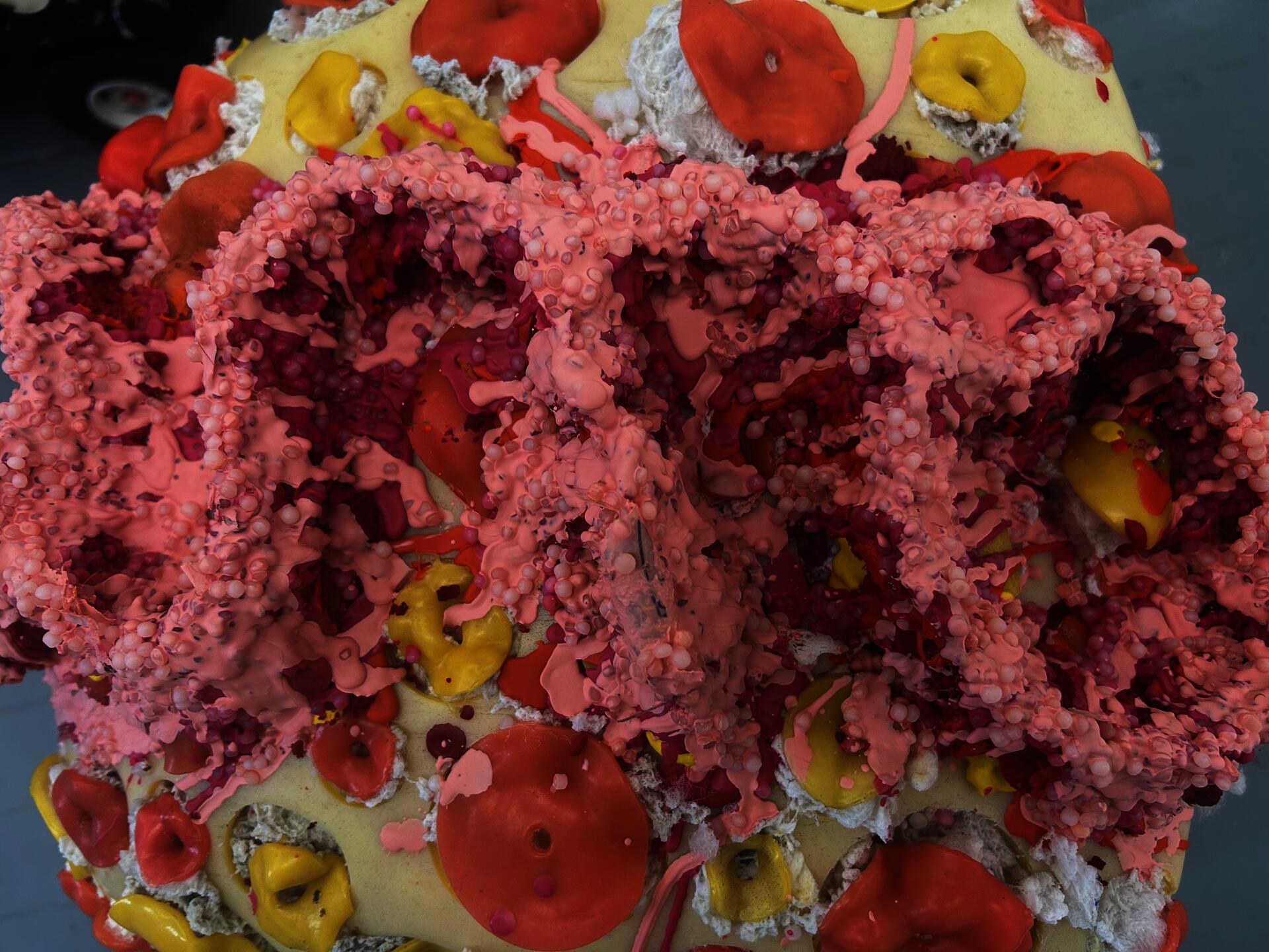Details of the top of the yellow and orange car. Mirrored cursive script of the "o" and "n" in "done." The lettering is build up of layers of melted, dripping crayon and stuffing pellets.