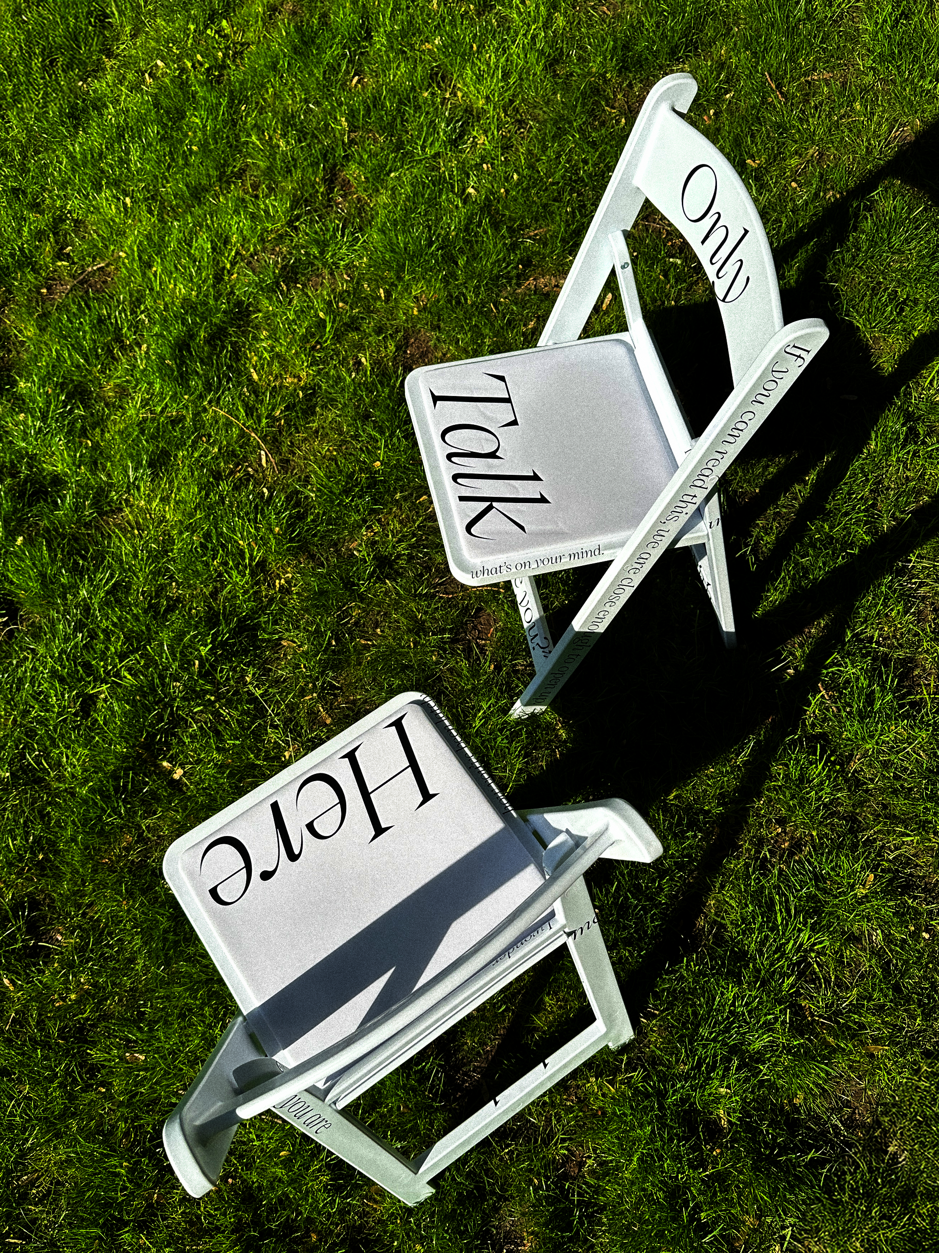 Two white chairs placed outdoors, printed with black text showing various conversation prompts.