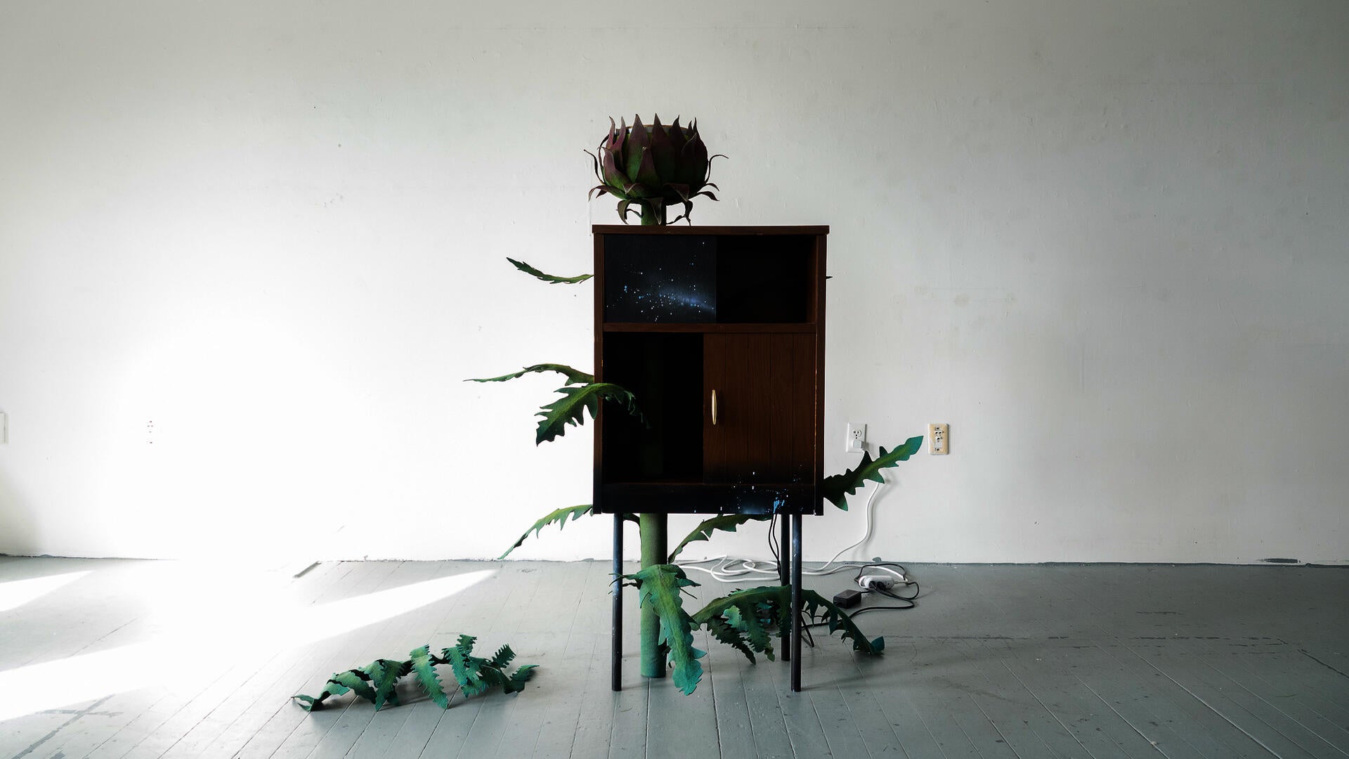 Cabinet sculpture with green felt leaves and a flower-like form emerging from the top.