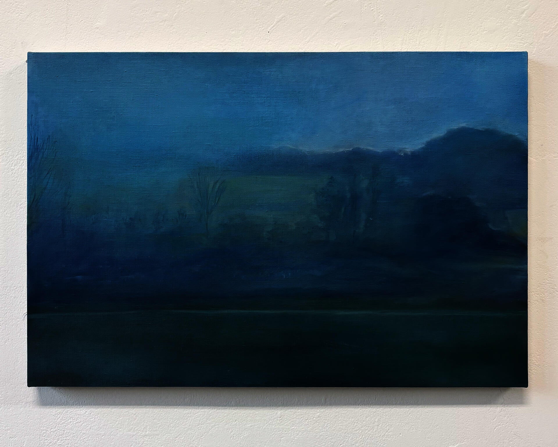 This is a painting of a foggy landscape, with a little bit of light just along the treeline. The fog is brilliant blue and the ground is a dull green.