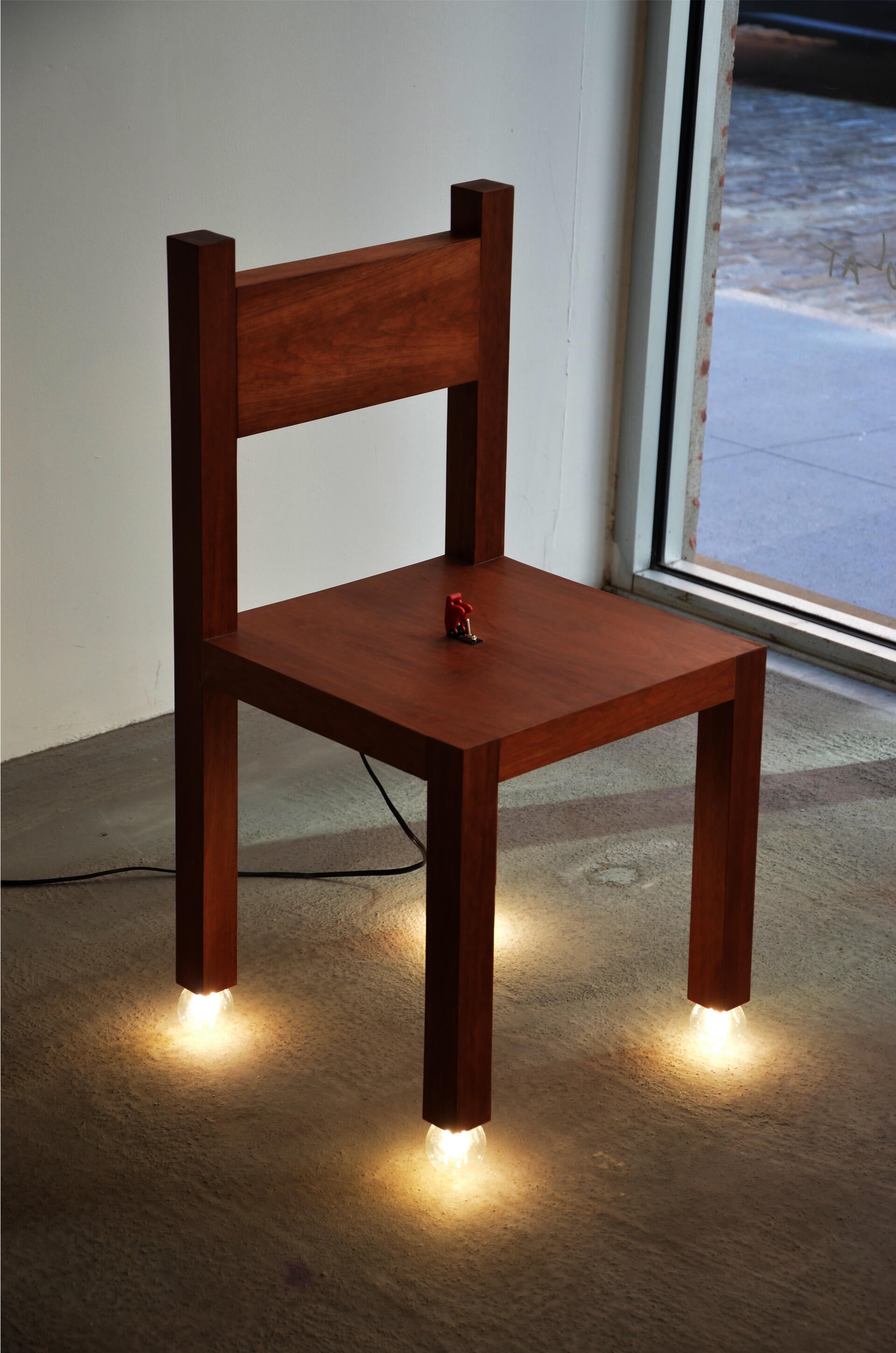 Cherry Chair with four light bulbs as its feet and a red switch in the seat, combining a chair and a lamp.