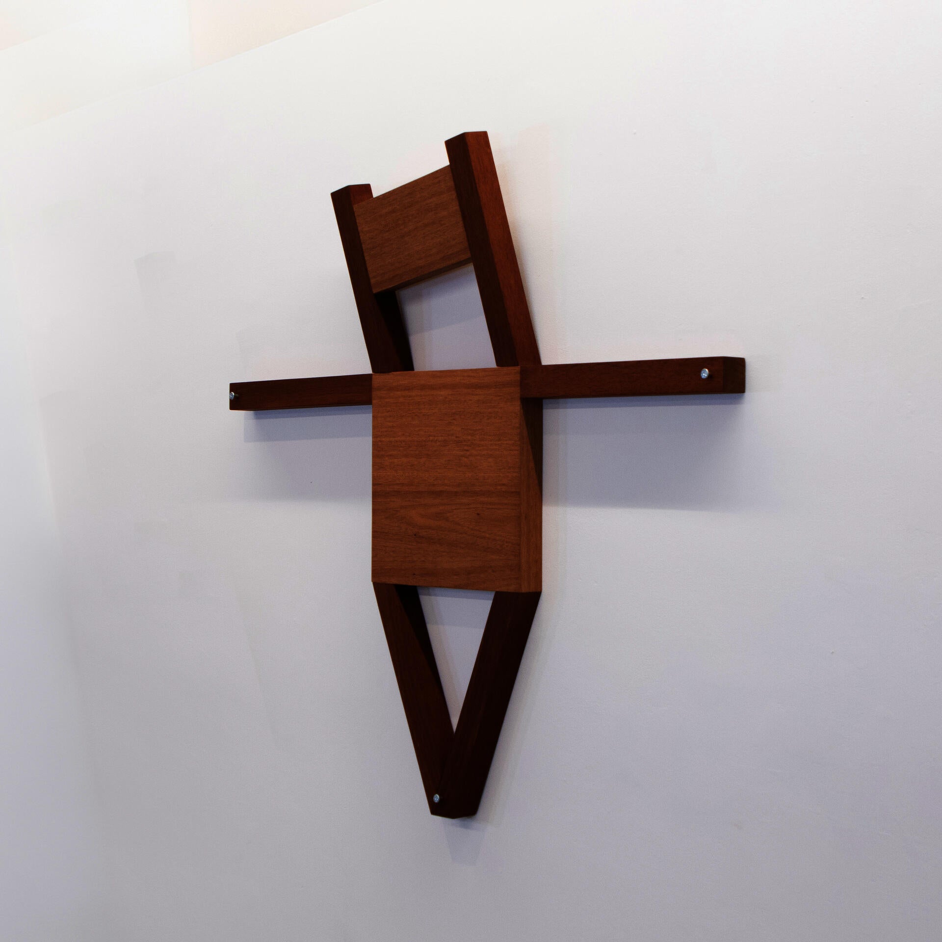 A mahogany chair transformed into a cruciform figure, combining the form of furniture with the posture of a crucified body.