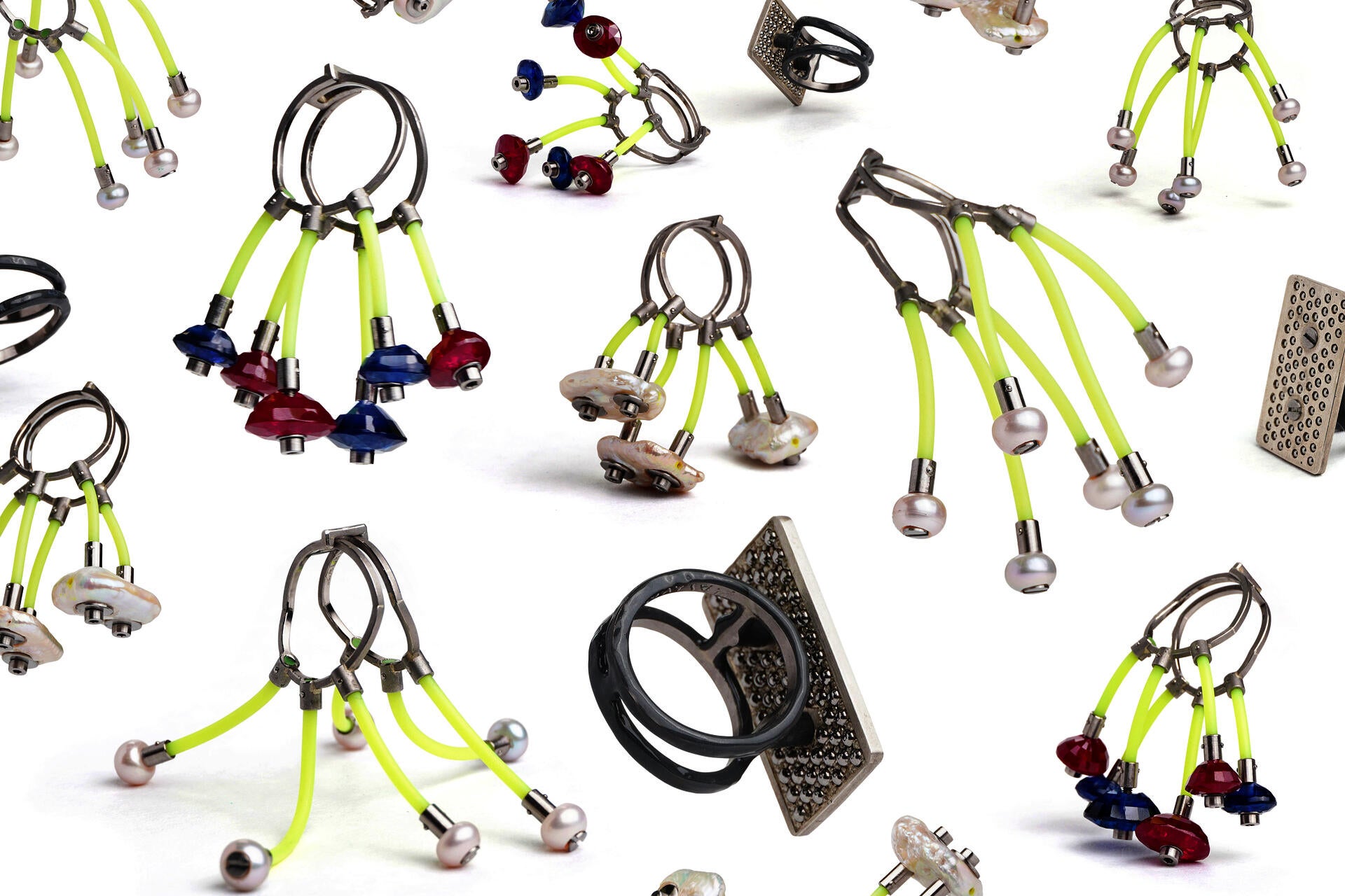 A composite image of four rings pictured from sixteen different angles on a white background. The rings have pearls, sapphires, or silver panels bolted onto bright yellow lengths of rubber that are connected to the ring shanks made from loops of square wire.