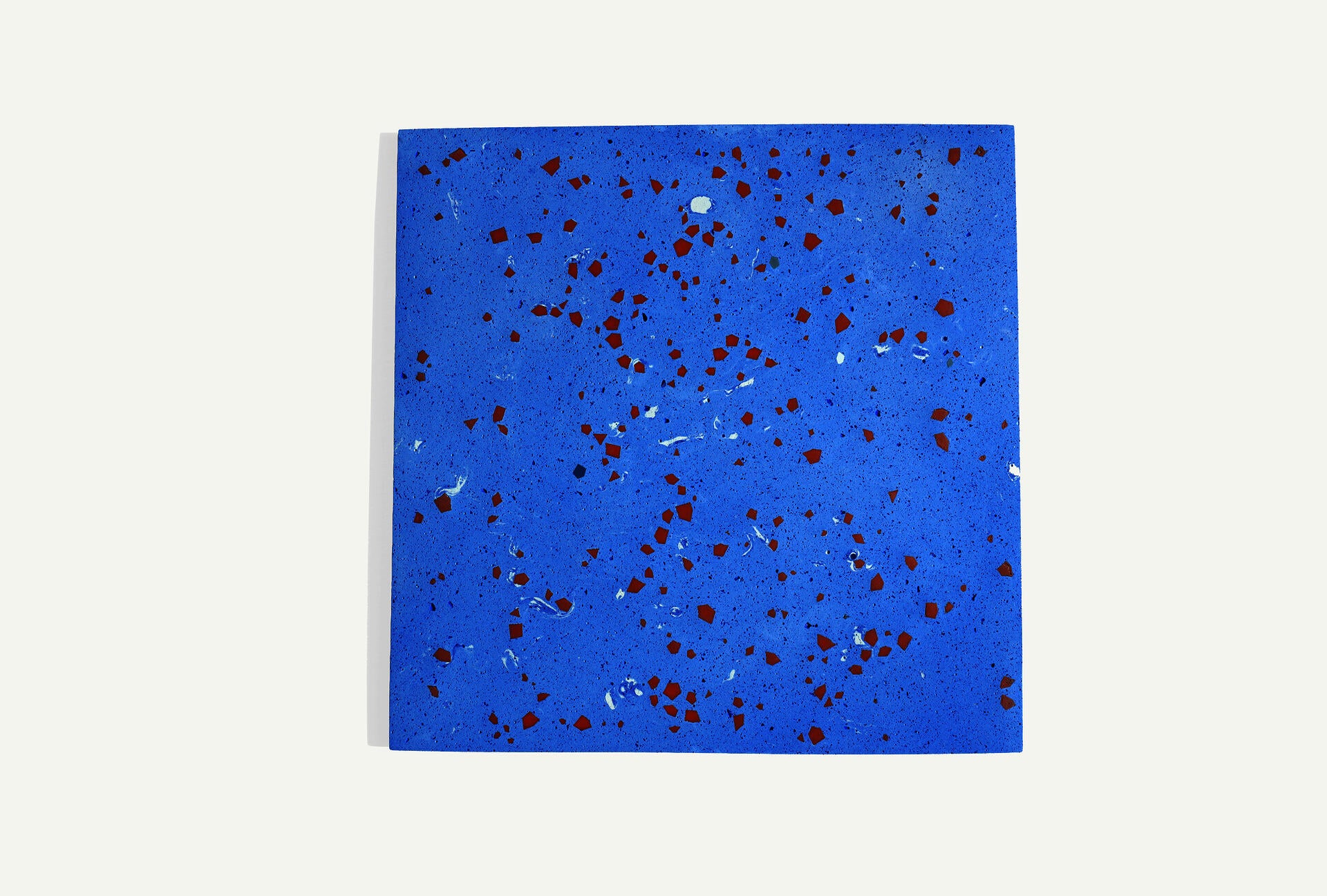 A single square pale blue terrazzo tile embedded with geometric fragments scattered across its surface.