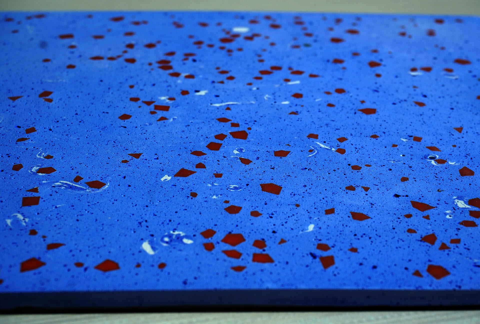 Side-angle close-up of a pale blue terrazzo tile showing depth and terracotta geometric fragments embedded in the surface.