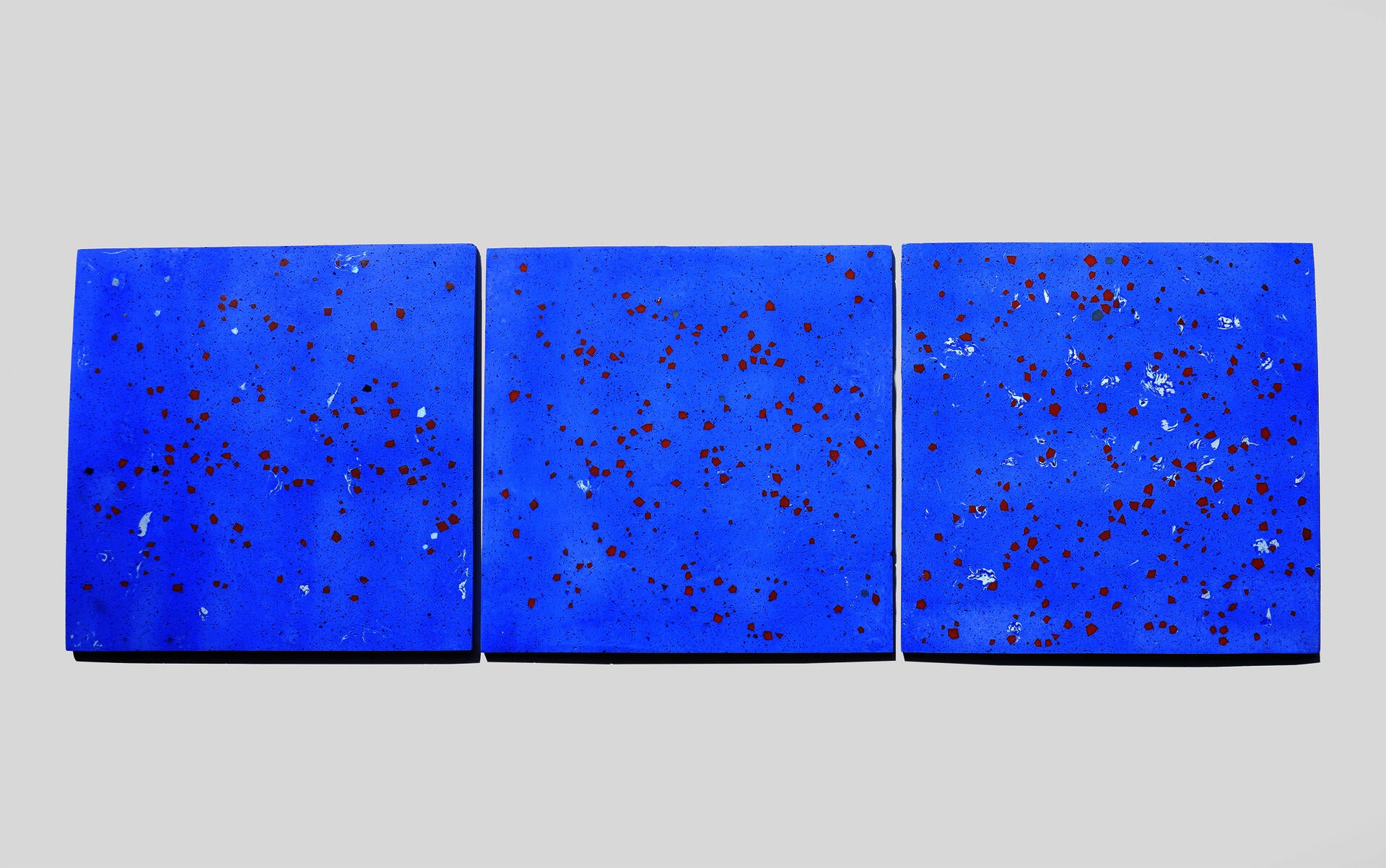 Three square pale blue terrazzo tiles arranged side by side, each embedded with scattered colored geometric fragments of varying sizes and shapes.