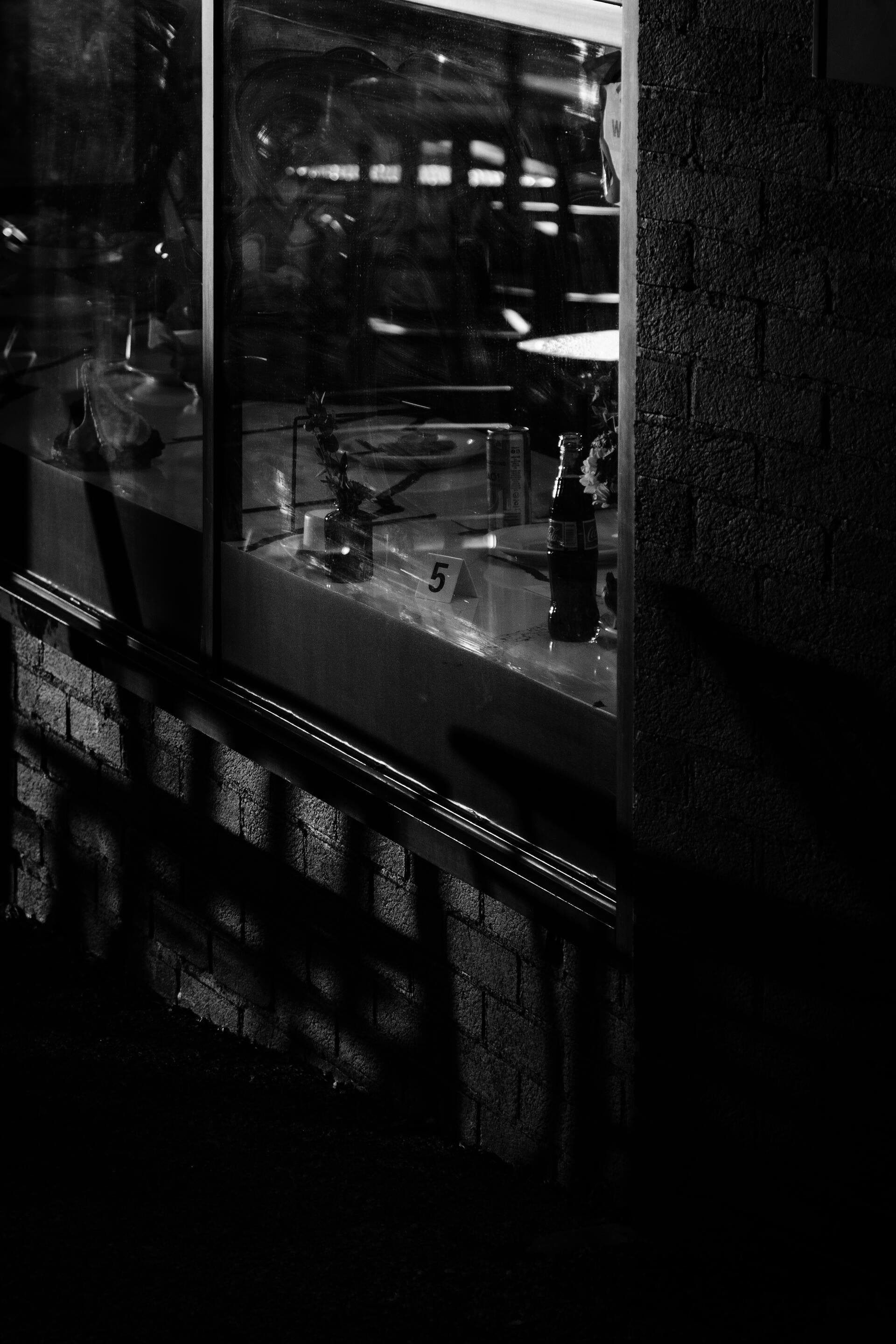 Restaurant window reflection showing a order number and a Coke bottle, black and white photography with brick facade.