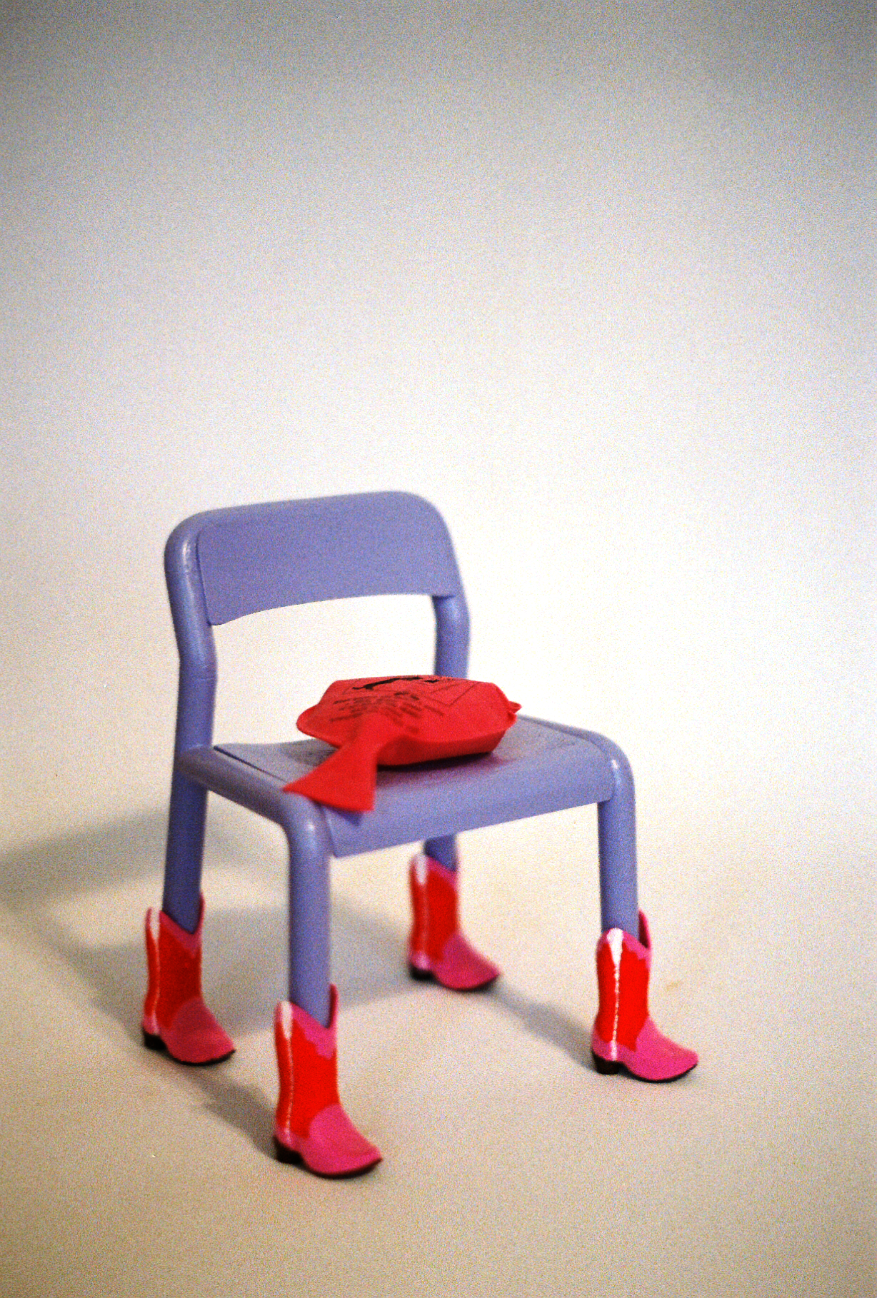 35mm film photograph of a 7" model of a lavender painted Ikea chair wearing pink and red cowboy boots and a whoopee cushion on the seat.