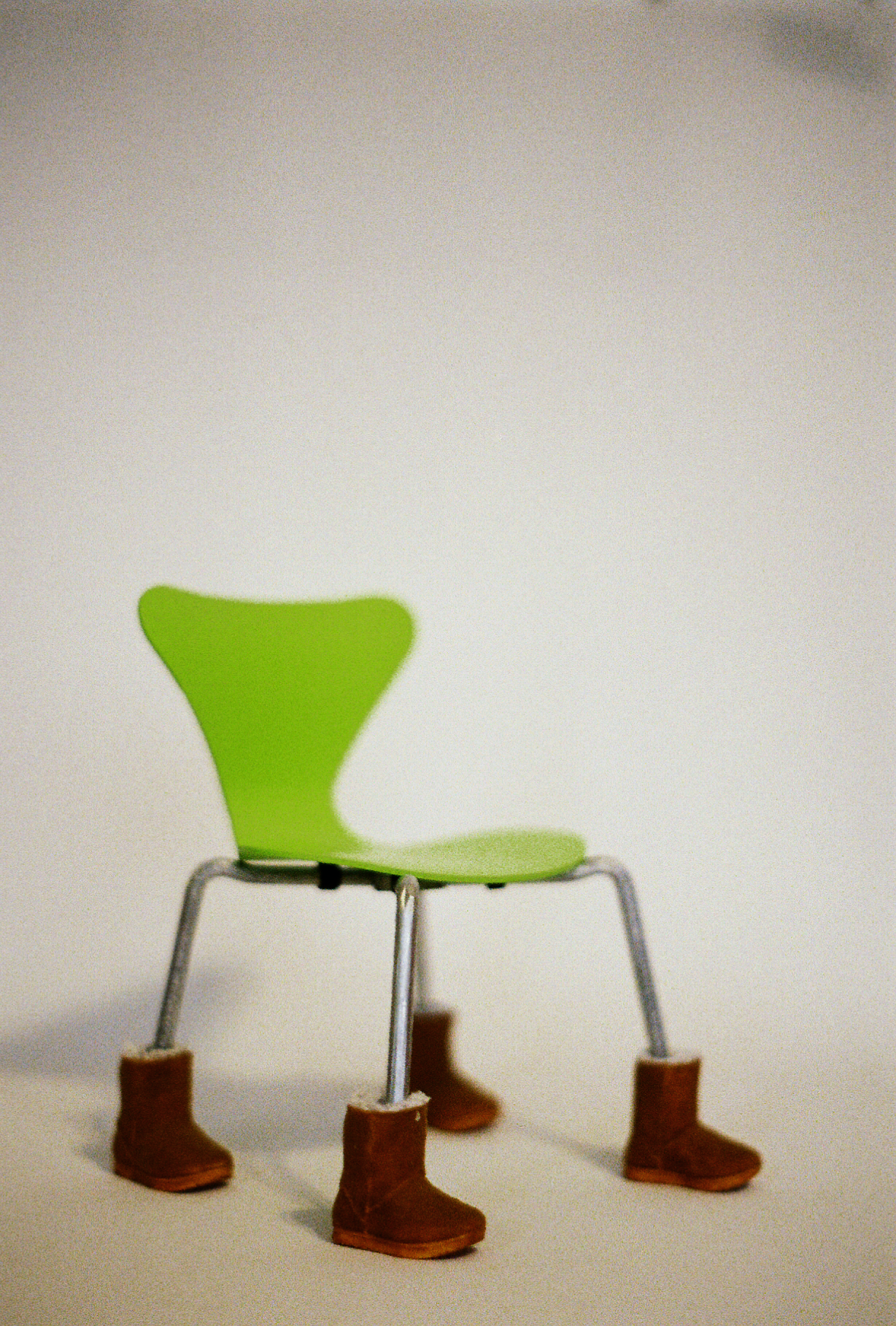 35mm film photograph of a 7" model of a neon green Series 7 chair wearing Ugg boots.