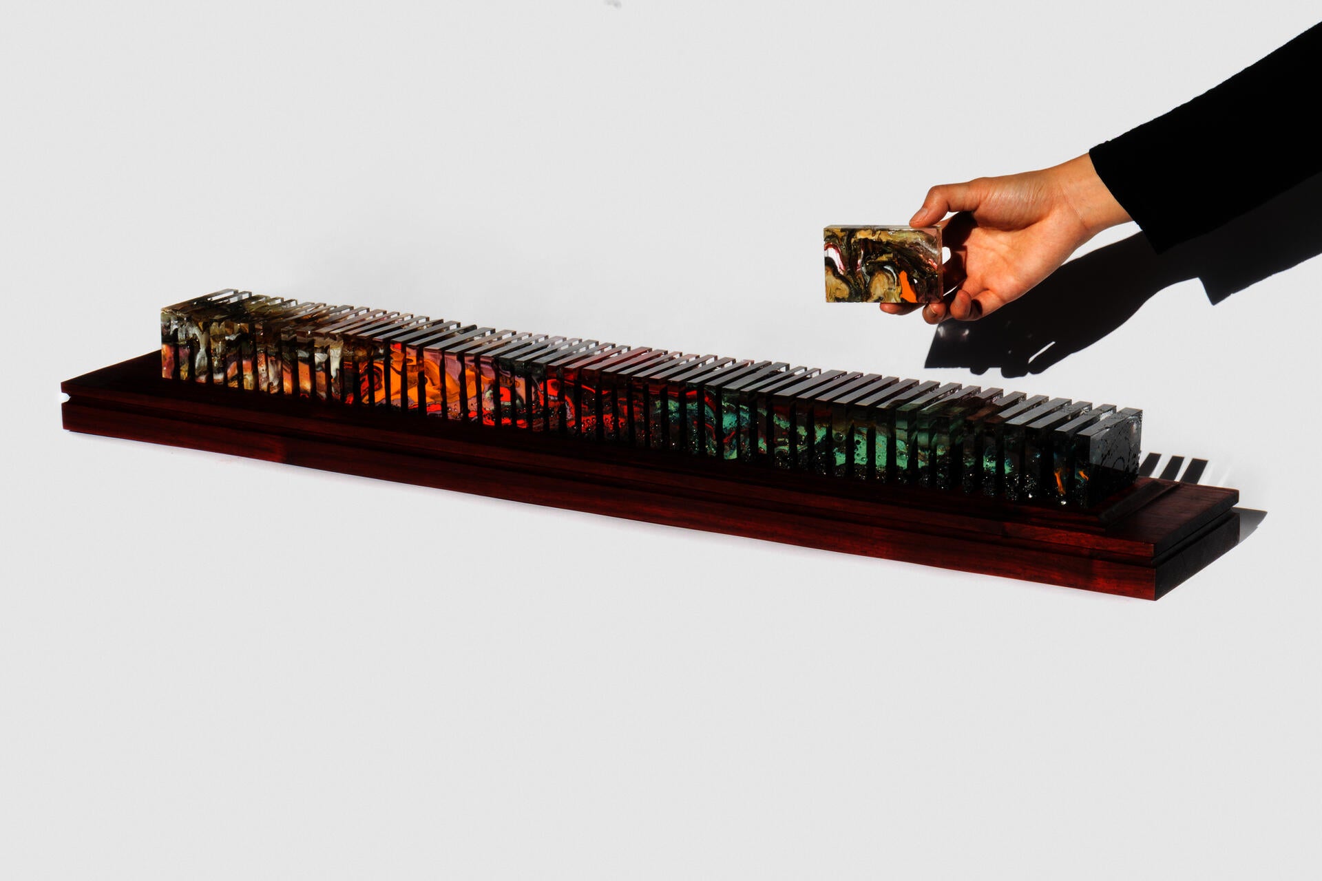 Fifty-three polished glass slices displayed on a long padauk platform showing both gaps and continuation at the same time. 