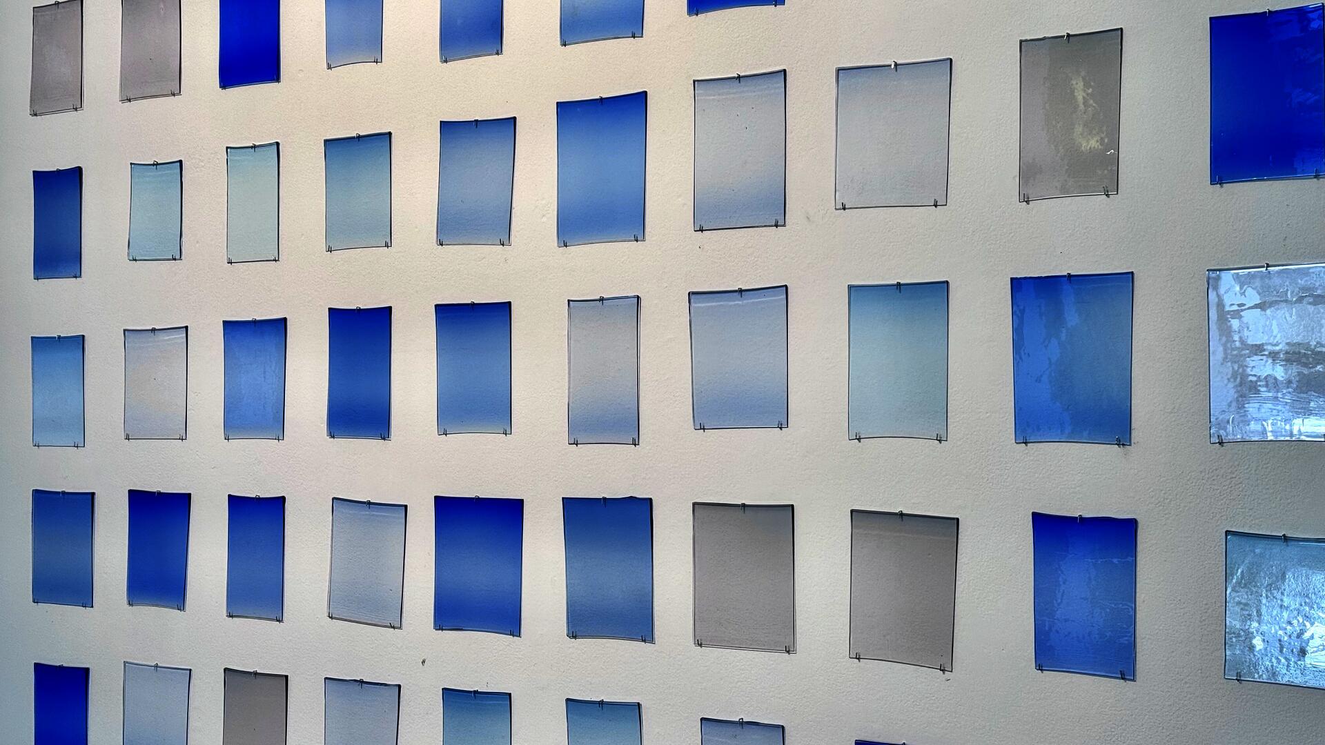 Grit of rectangular glass panels mounted on a wall, each showing subtle variations of blue gradients and transparency.