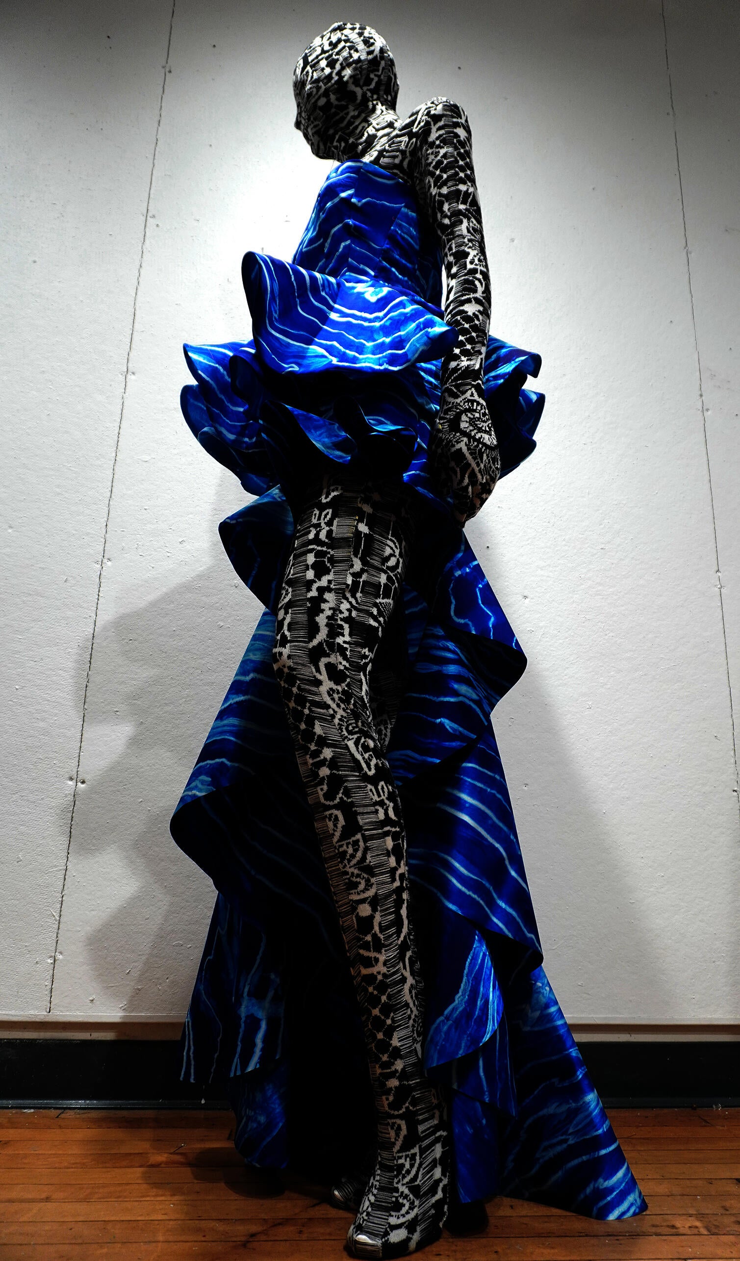 Mannequin wearing sculptural blue silk dyed dress with wave-like ocean patterns over black-and-white jacquard knitted bodysuit.
