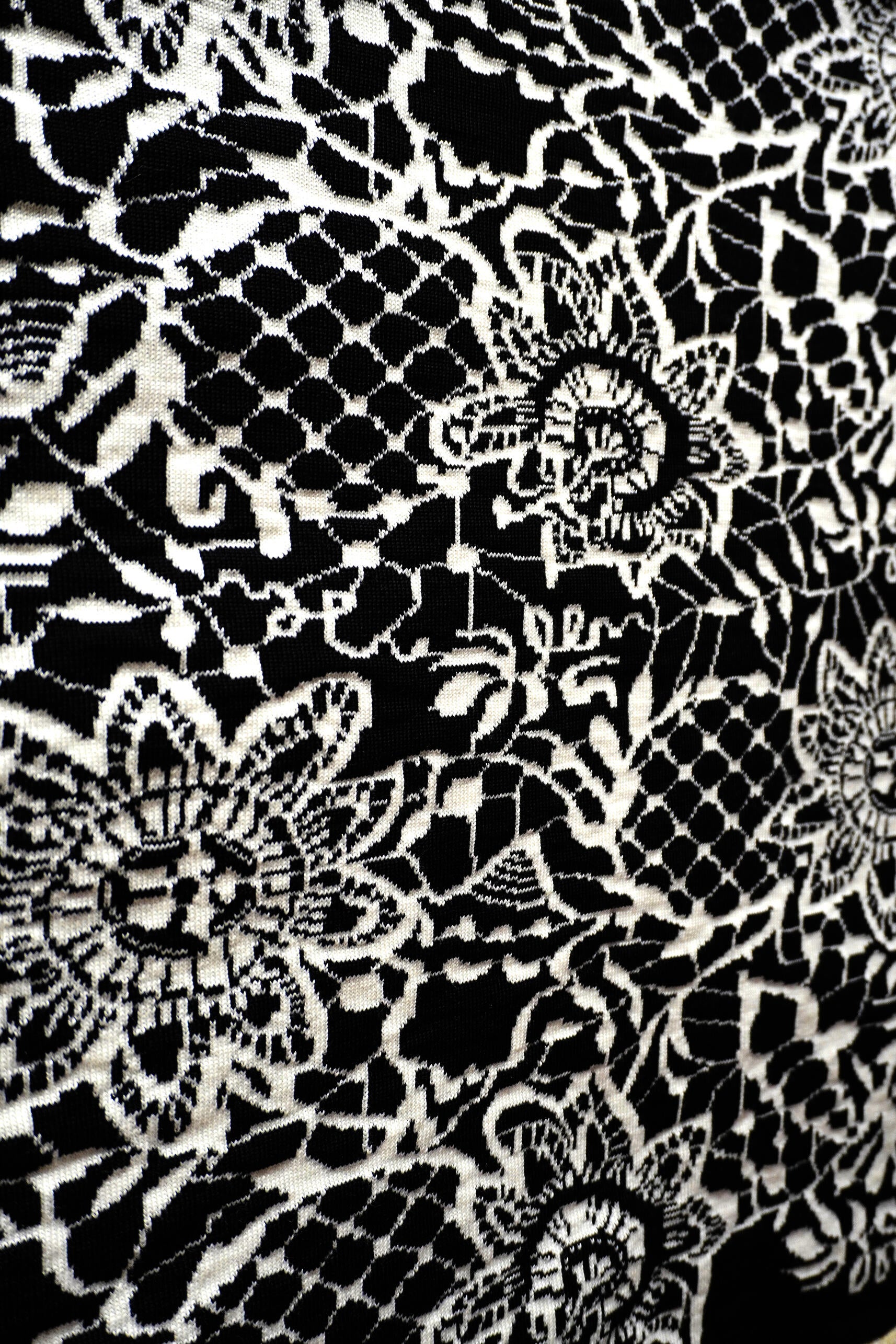 Close-up of black-and-white jacquard knitted textile resembling lace, with floral motifs and shells