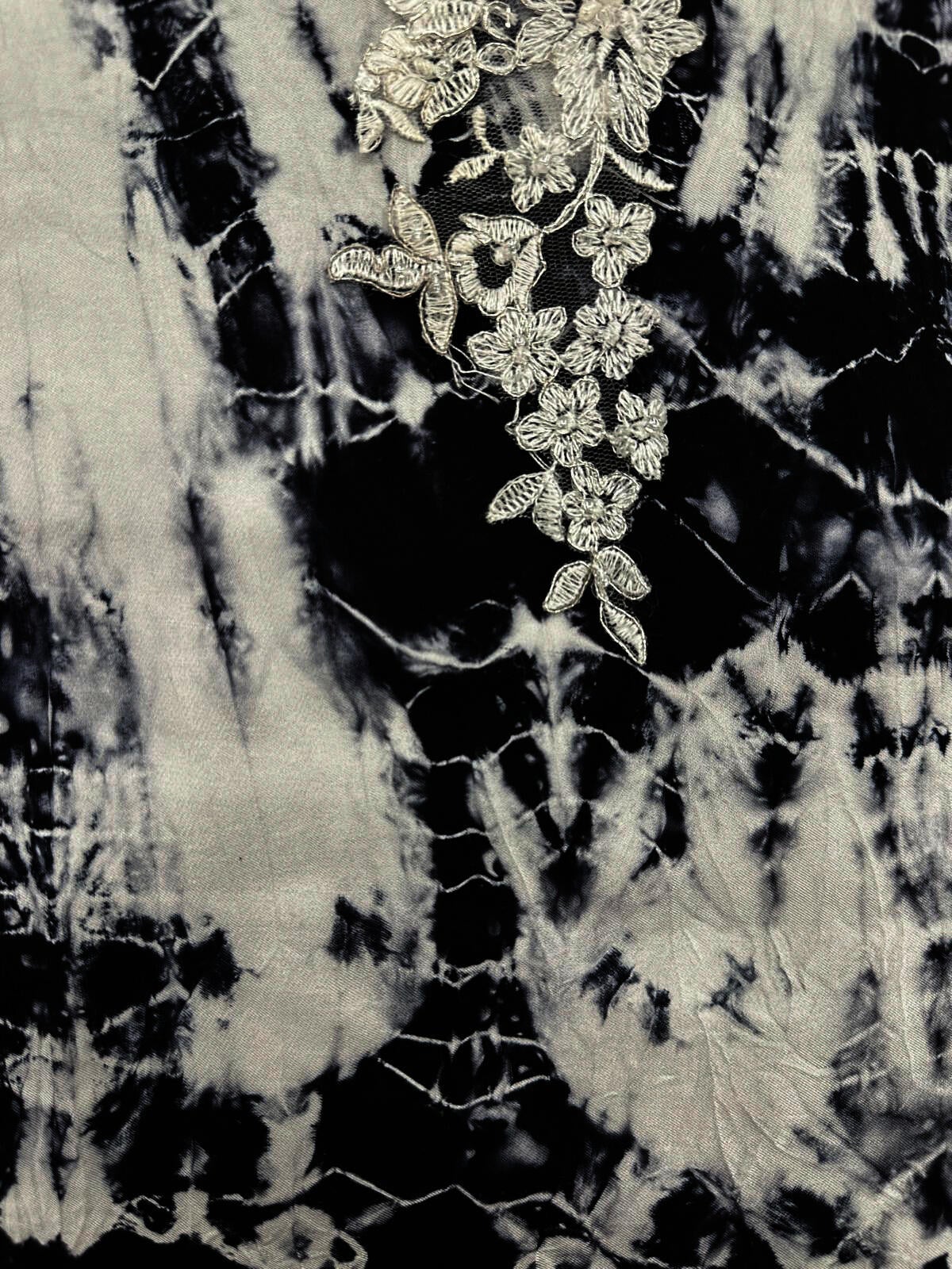 Close-up of black-and-white hand-dyed silk textile with white floral embroidery appliqué over sheer mesh