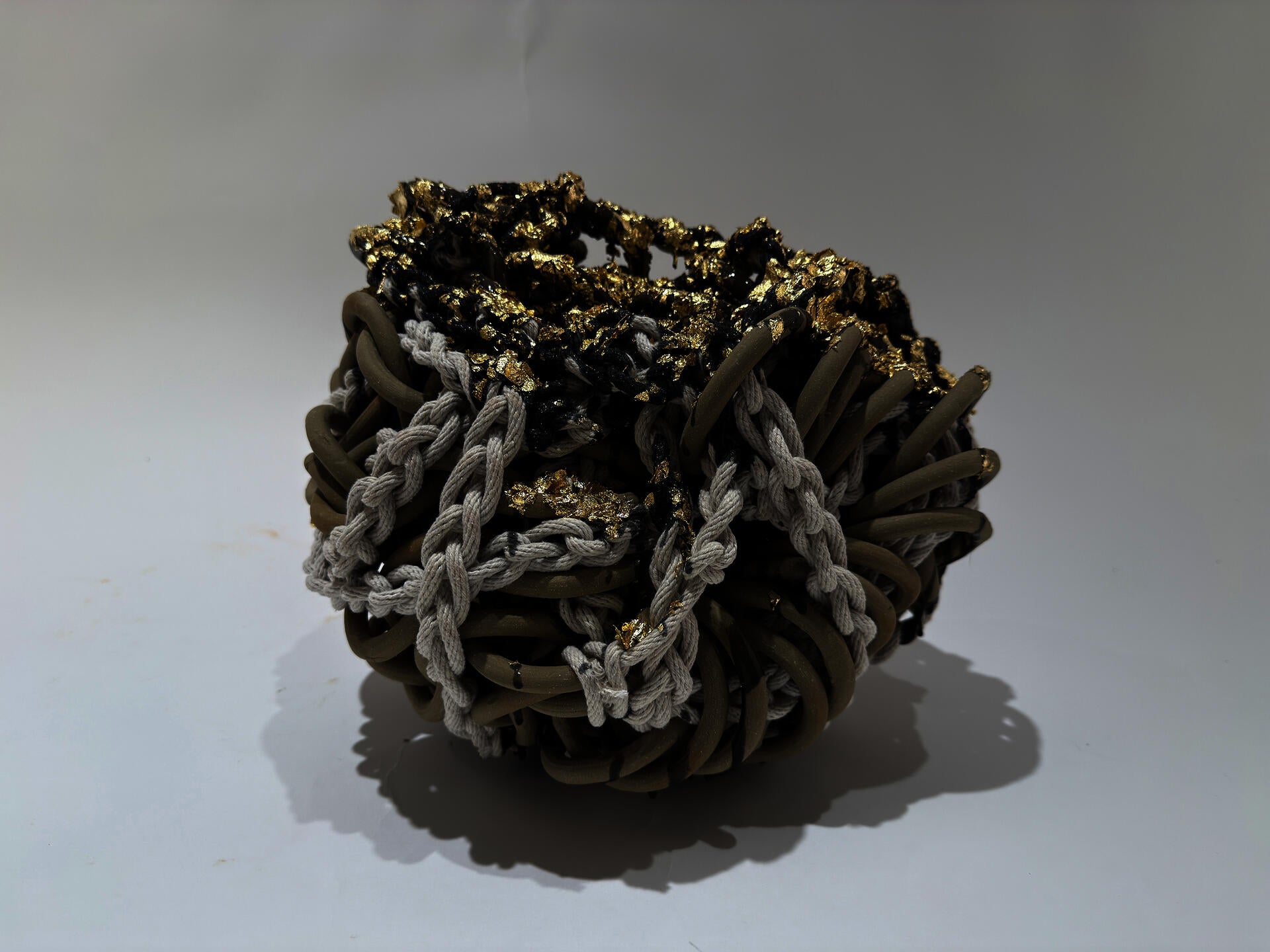 Smooth tan chainmail is wrapped in white rope.  On top blue latex is dripped and upon it is small bits of gold leaf sparkleing in a very dense work.