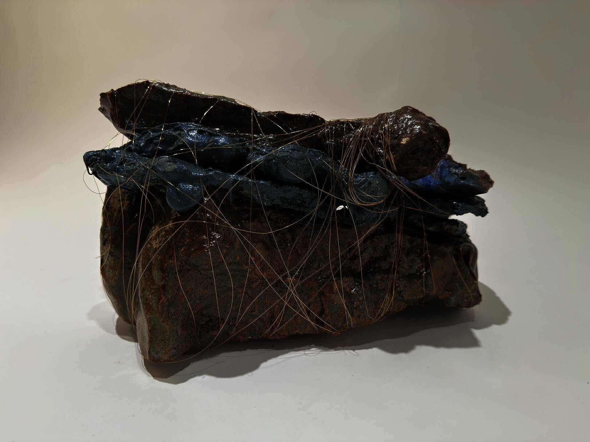 Three large smooth shiny glazed rock like pieces are faceted together with purple rubber.  The entire piece is wrapped with small copper thread as thin a hair.