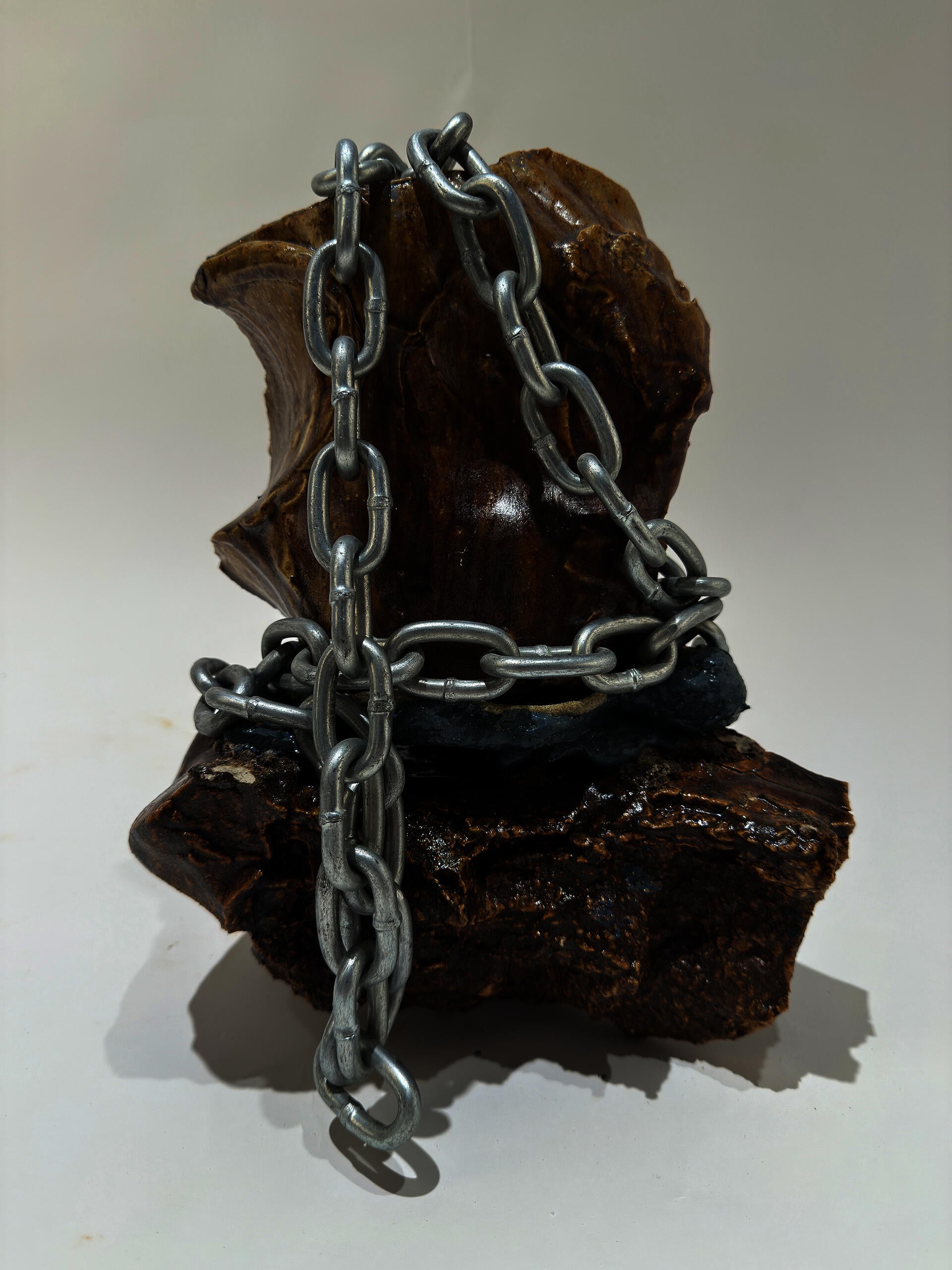 Several smooth rock like ceramic shards are faceted together with rubber.  A large steel chain wraps around the piece loosely but adds some weight to the object.