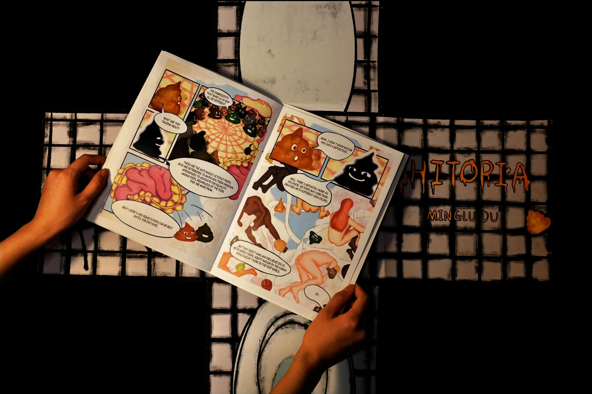 An opened interior page from the comic book Shitopia is placed on top of the foldable toilet-shaped cover.