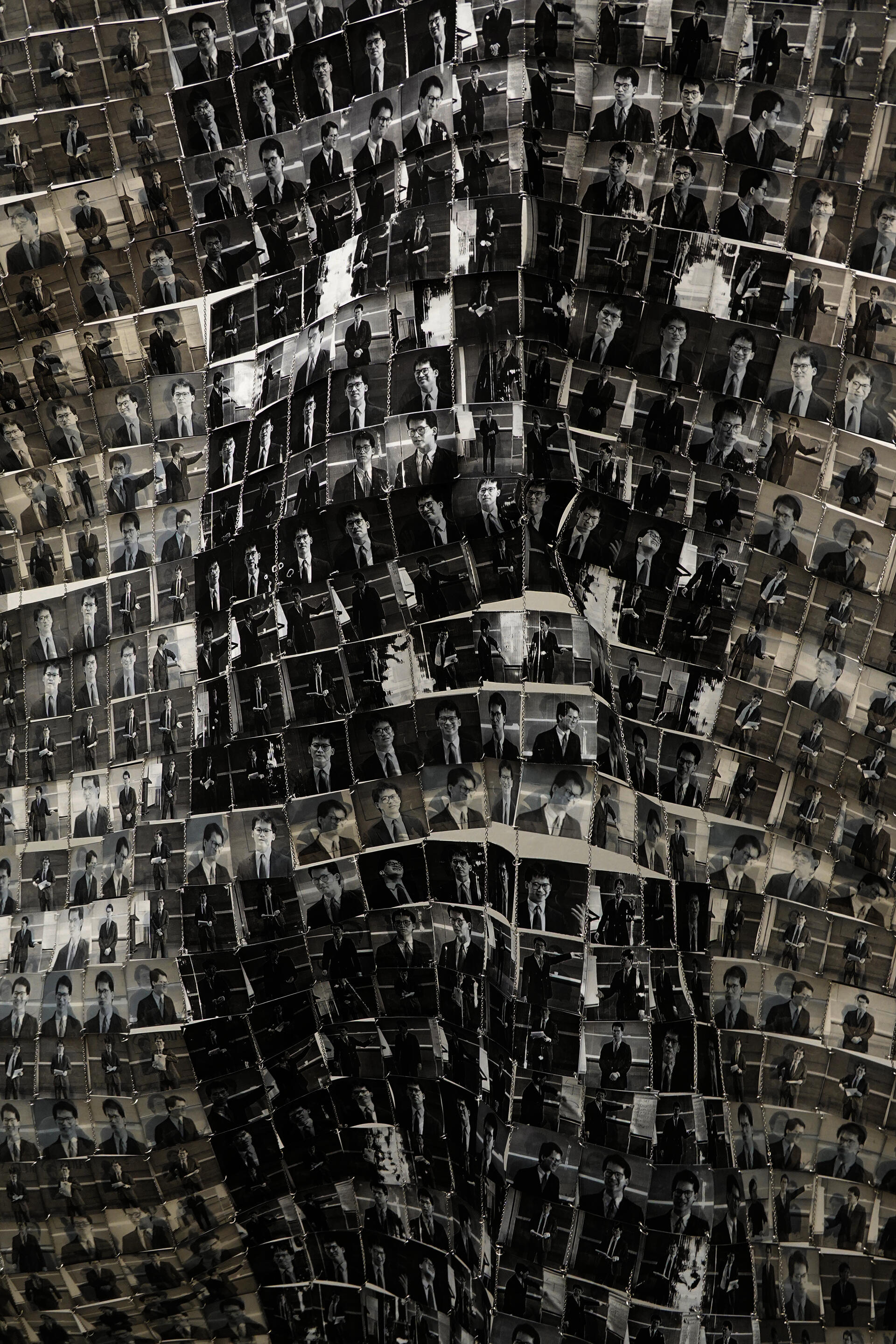 Close up image of black and white paper tiles that each have a portrait of a man in glasses.