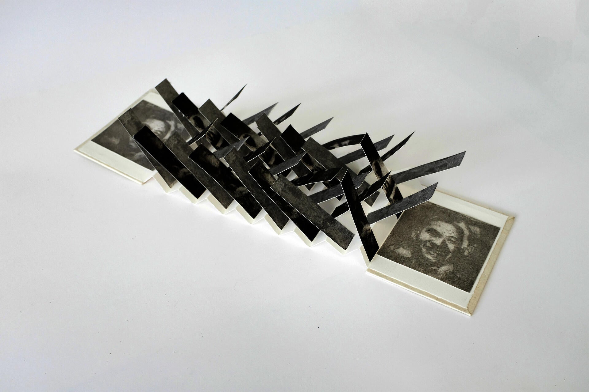 Open book with criss-crossing slips of paper. The slips display a distorted and monochrome male portrait.