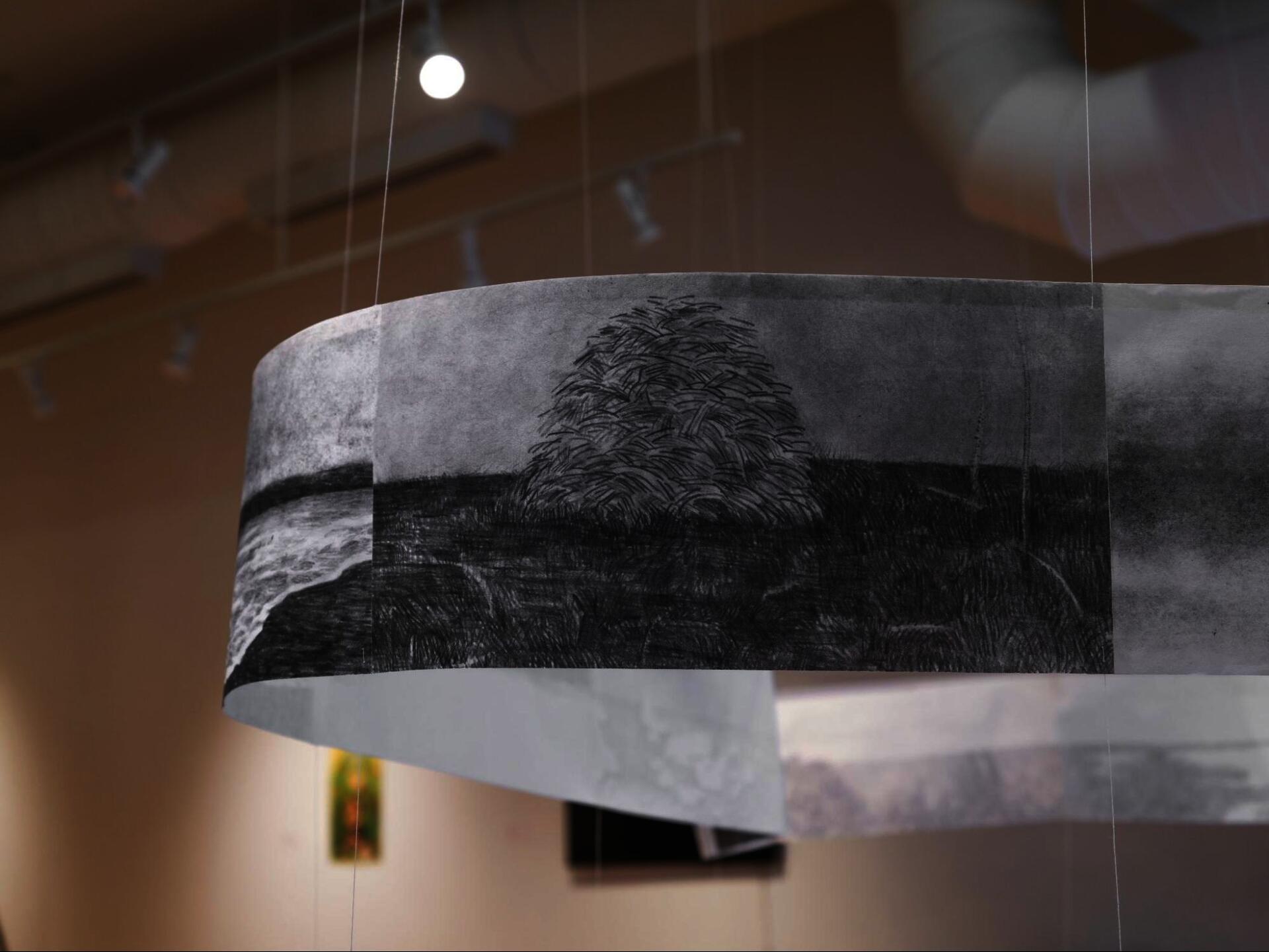 Close-up of a curved paper strip with charcoal landscape drawing, suspended by thin vertical strings