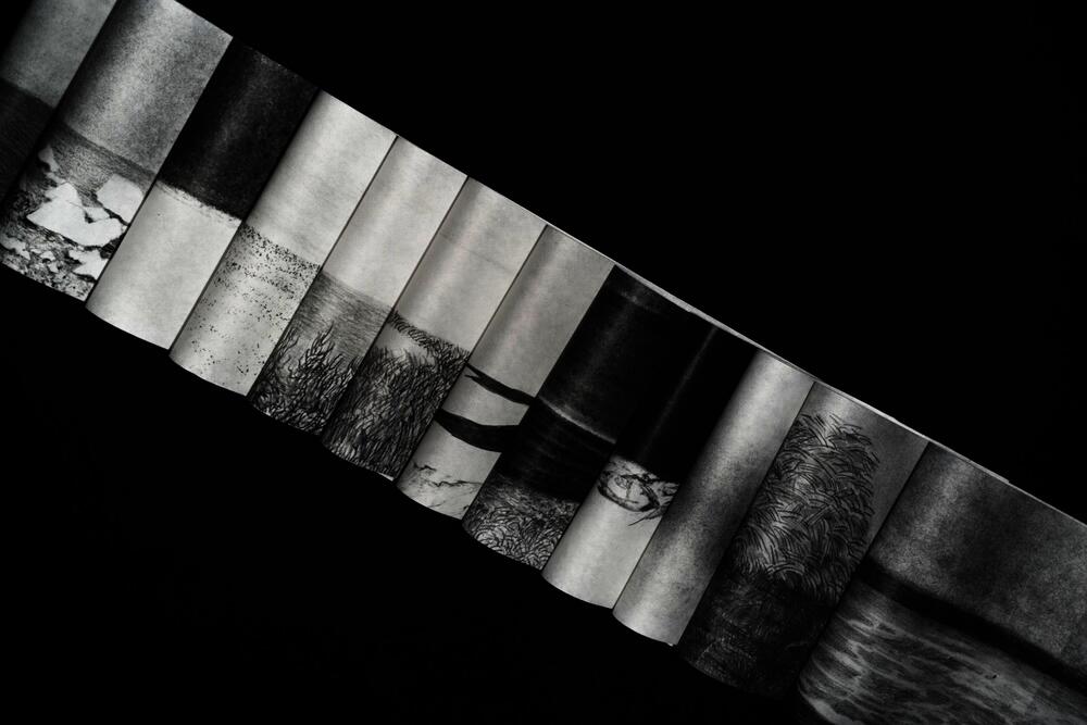 Accordion-folded paper strip with charcoal landscape drawings forming a continuous horizon against a black background