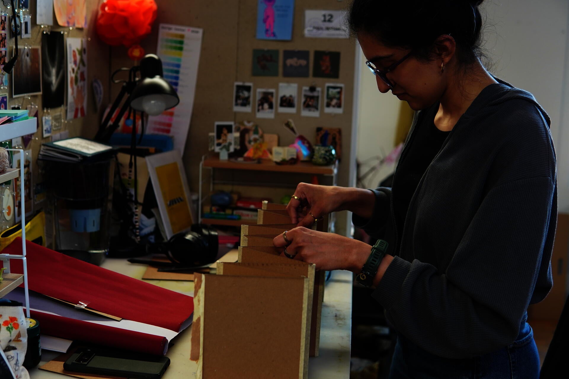 Image shows artist arranging an accordion fold mockup book made of scrap material as a prototype for her final.