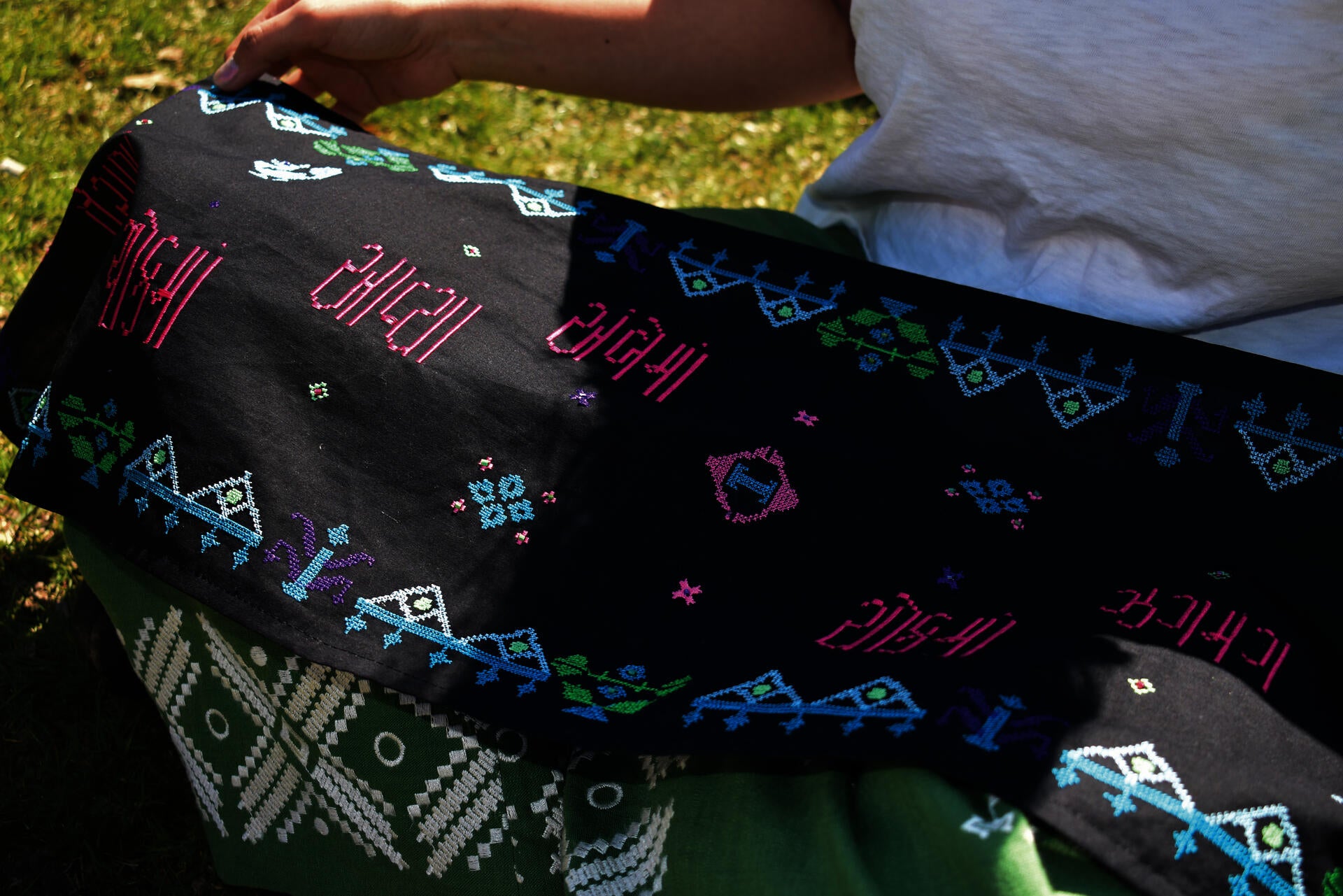 A digitally embroidered scarf displays the Moti typeface in vibrant pink, blue, green, and white threads on dark fabric, featuring Gujarati script and geometric beadwork-inspired motifs scattered across the textile