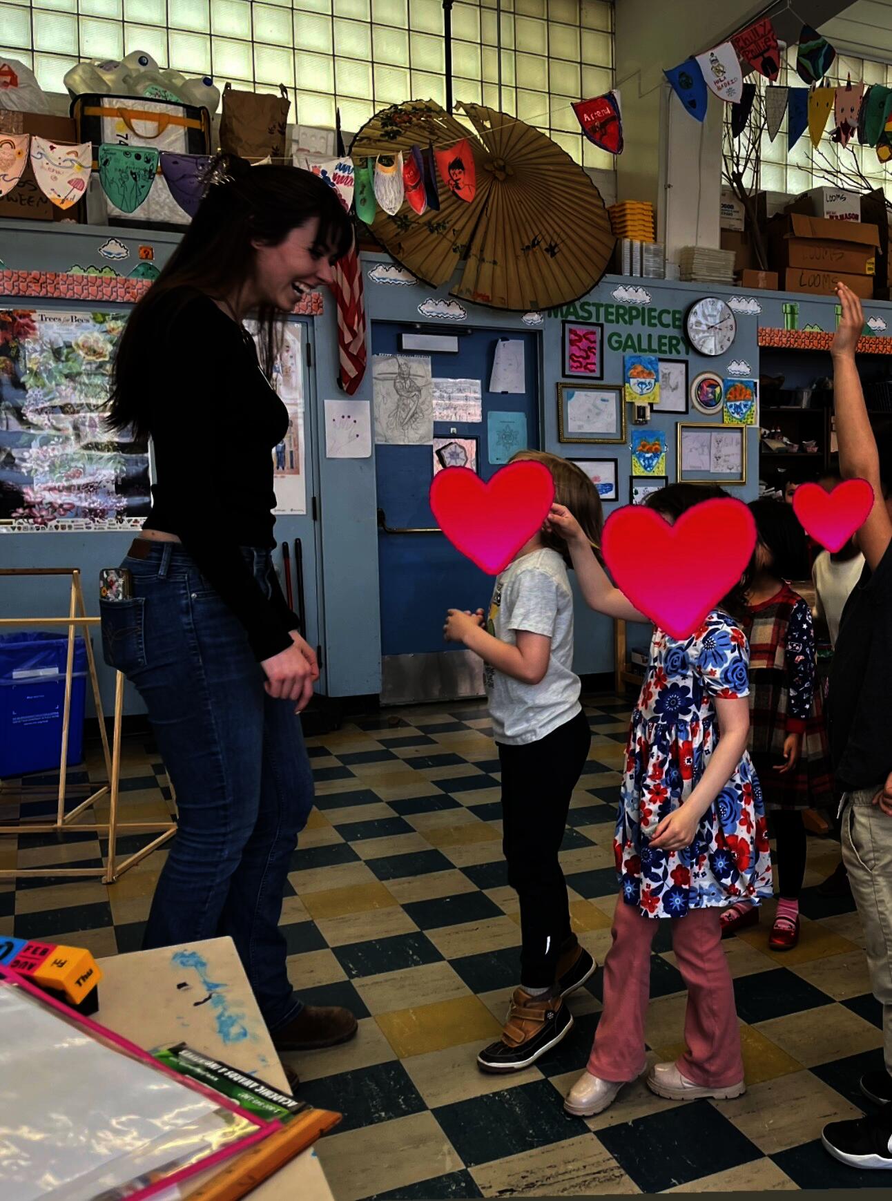 students rush up to a teacher at the front of the classroom jumping up and down with their hands raised