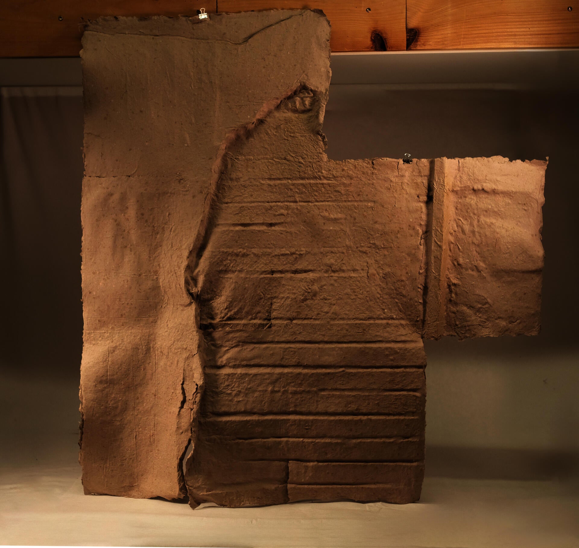 A sheet of handmade paper cast from a basement wall, showing the impressed texture of crumbling plaster, wooden lathing, and brick.