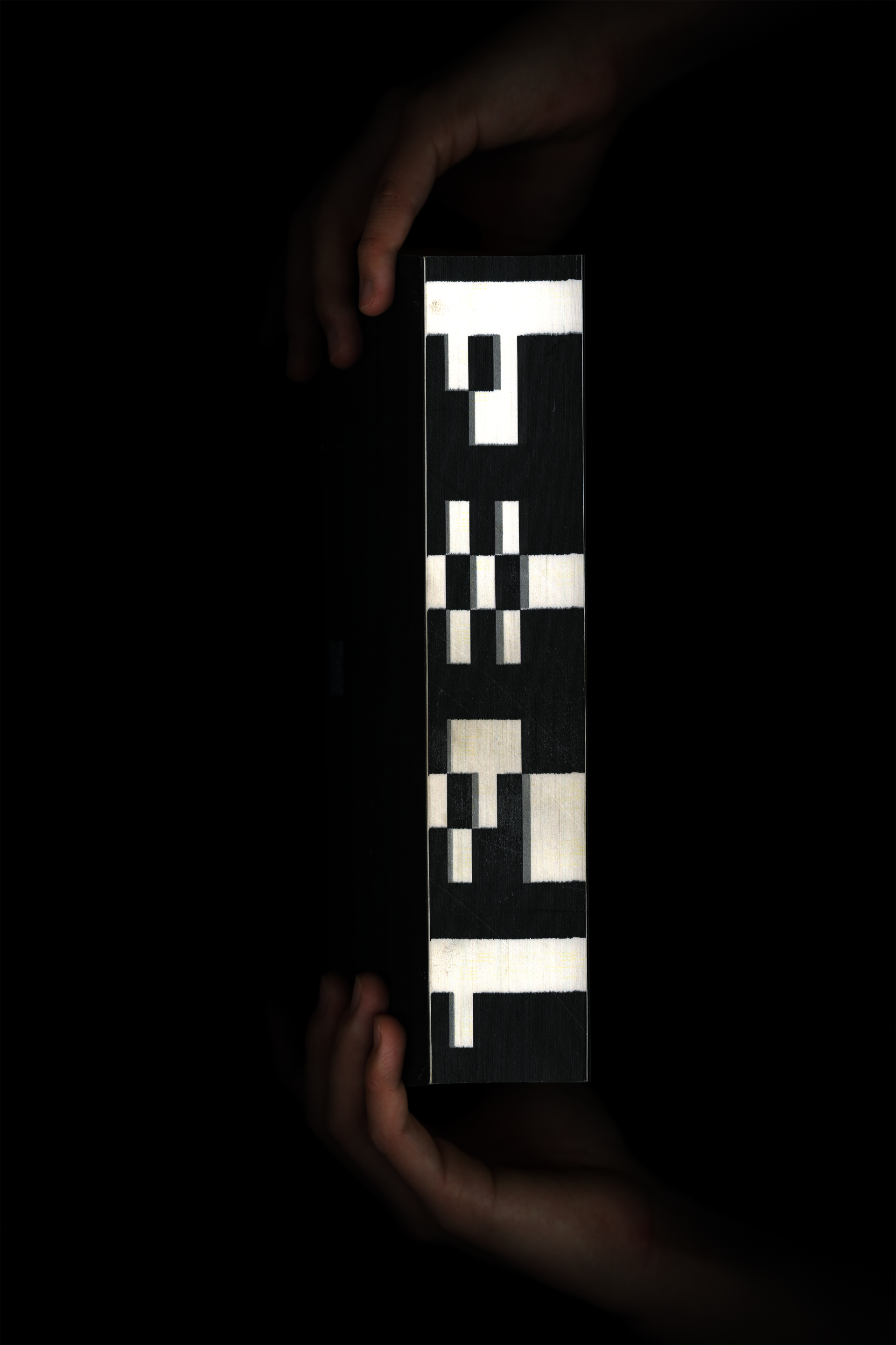 Hand holding a black book titled "1984" on the fore-edge. There is a QR code and an encoded title on the cover of the book.