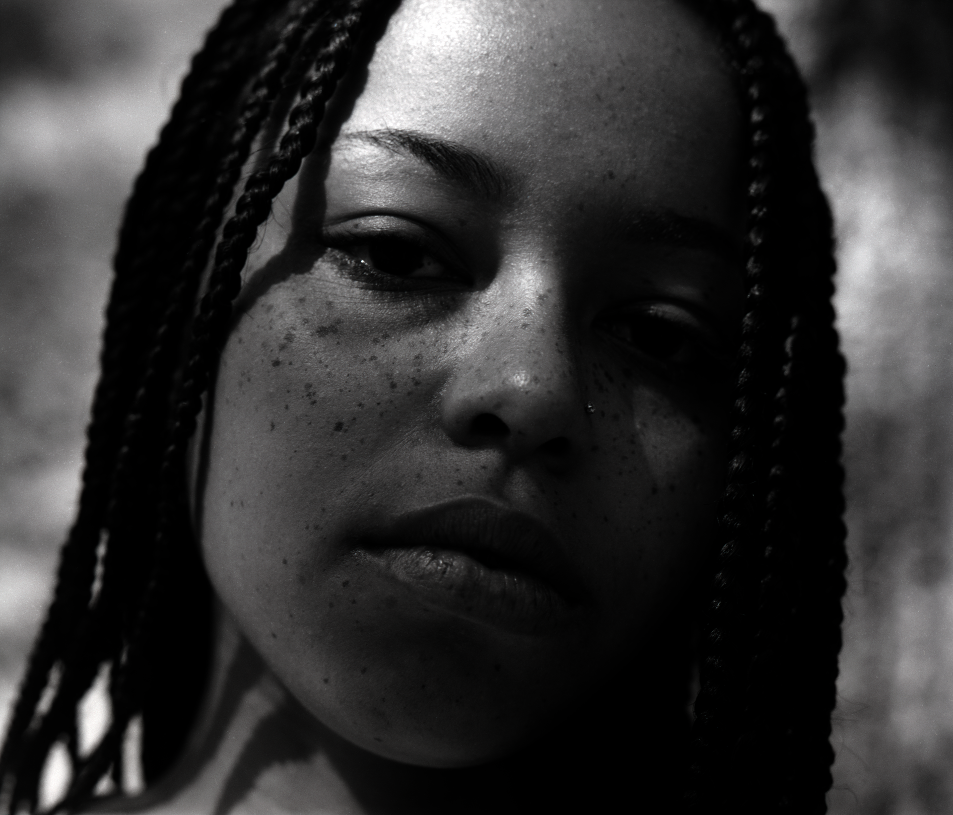 Black and white close-up photograph of a person with braided hair and freckles. Their expression is calm and introspective, conveying a serene and thoughtful mood.