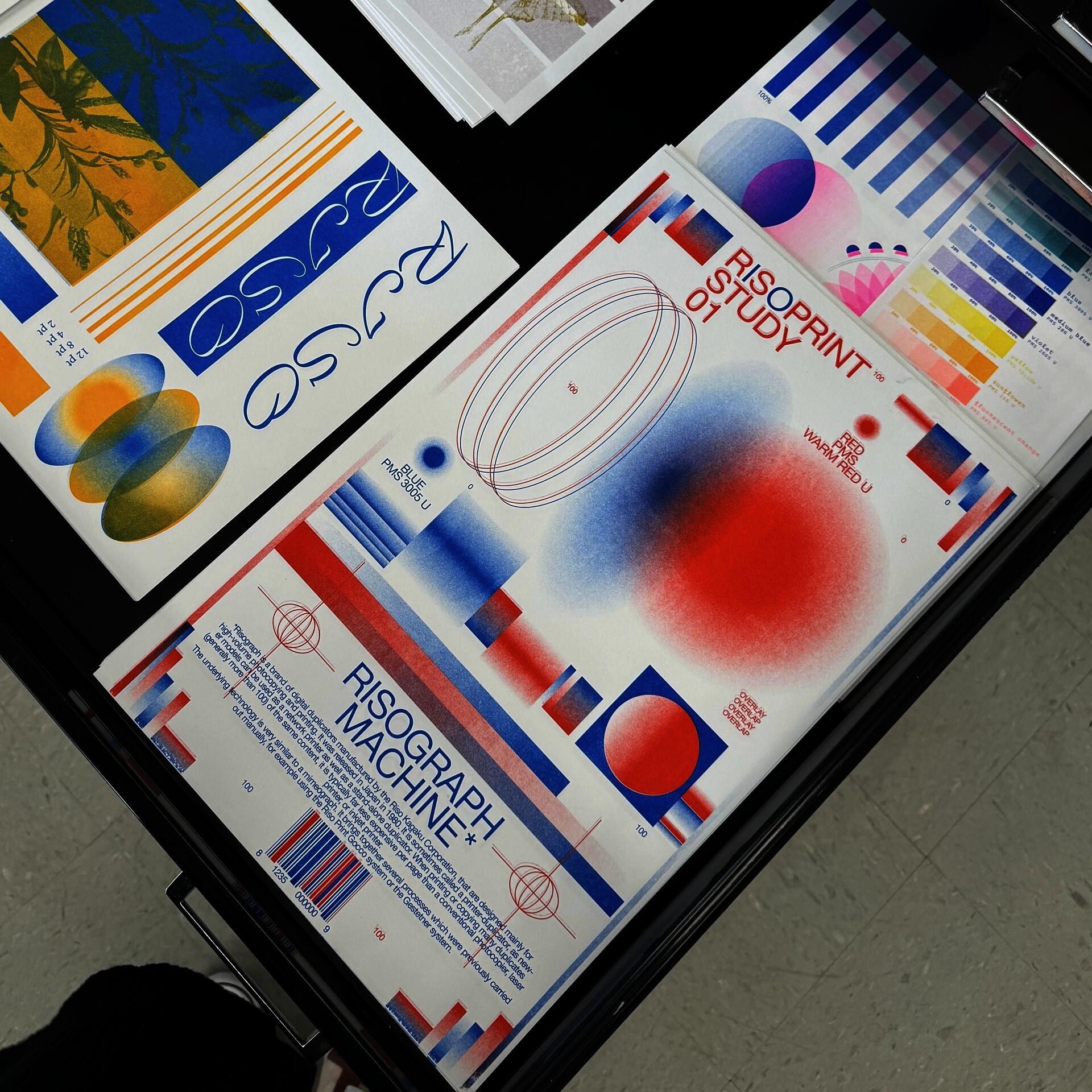 Overhead view of riso-printed poster titled "Risograph Machine" on a table, showing layered blue, red, yellow, and pink gradients, type experiments, color swatches, and geometric forms.
