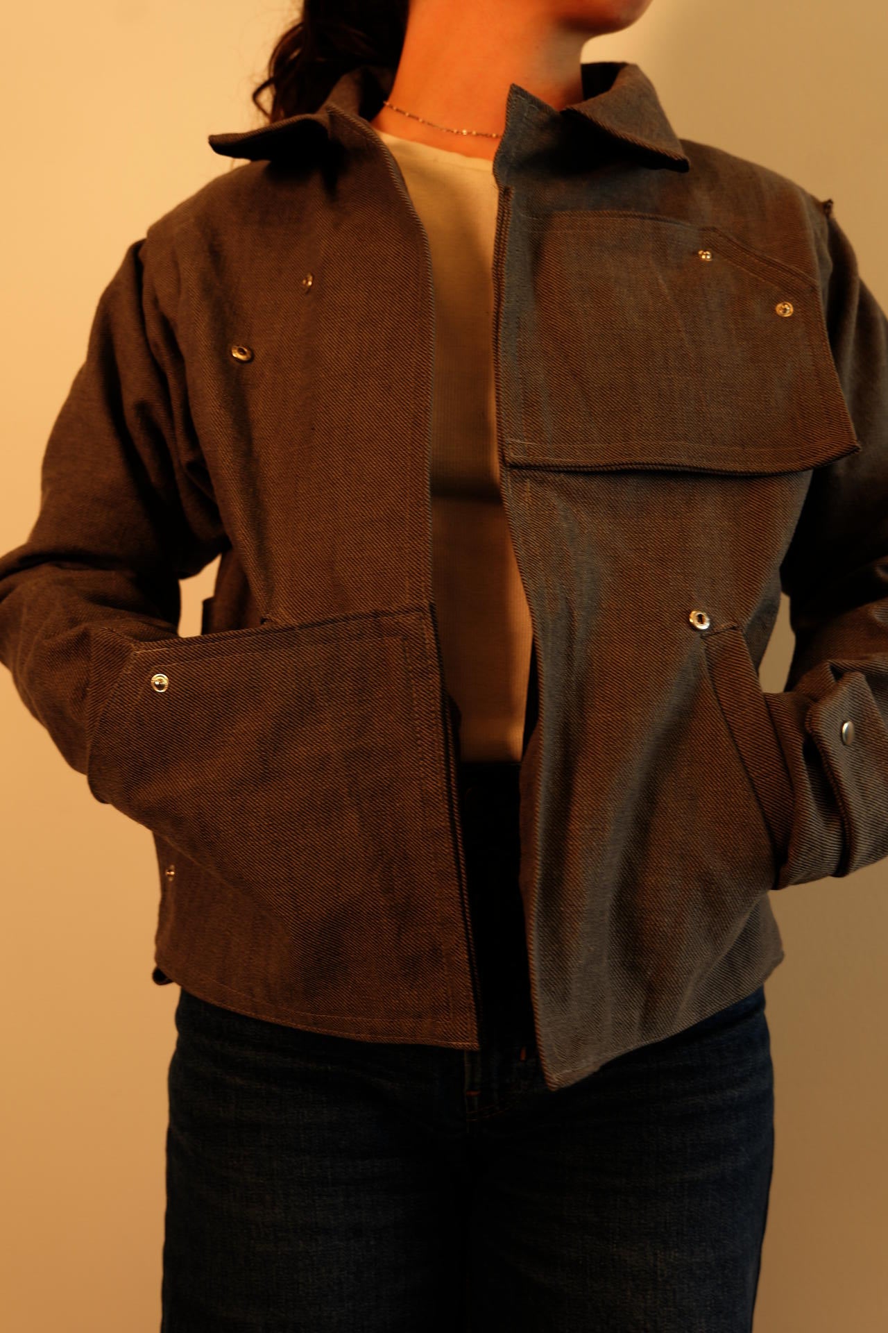 Teammate is wearing a finished grey  jacket made from a repurposed IKEA sofa cover, with silver snap hardware visible across the chest, lower pockets, and cuffs.
