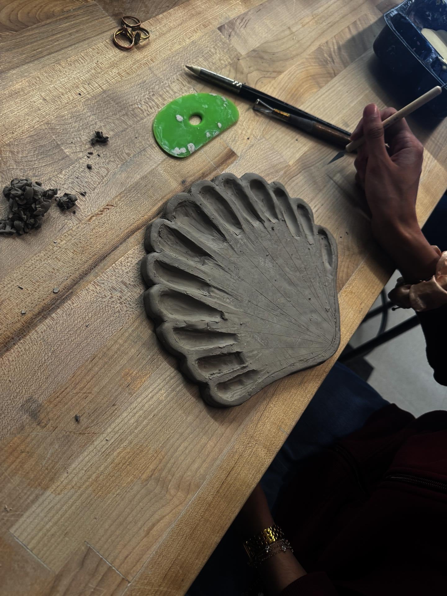 A student out of frame carves a ceramic sea shell into a paint palette