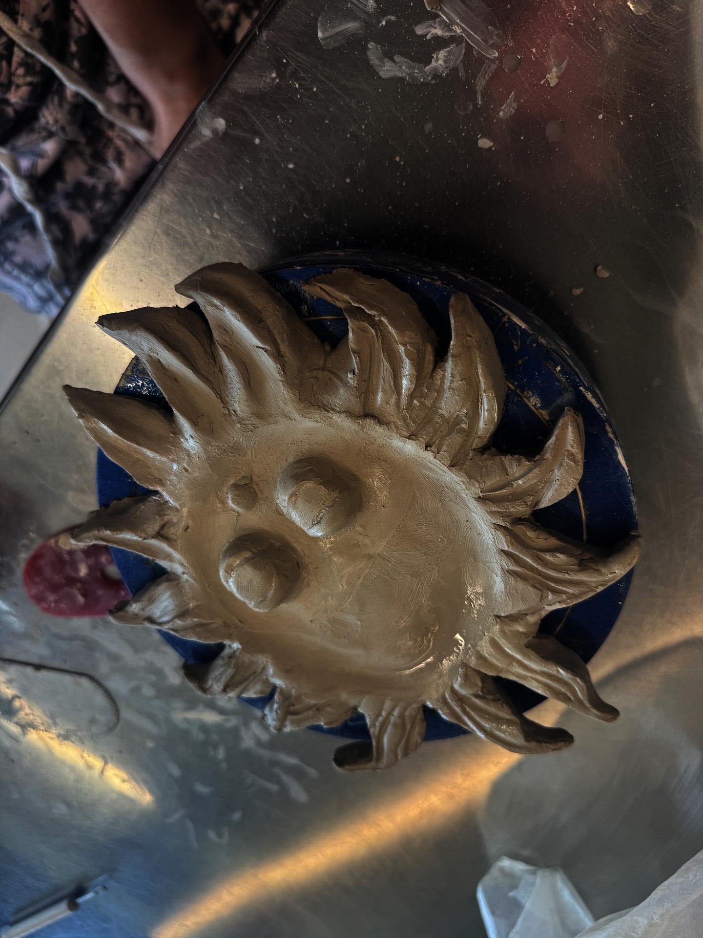 A student out of frame carves an incense holder shaped like a sun with a face