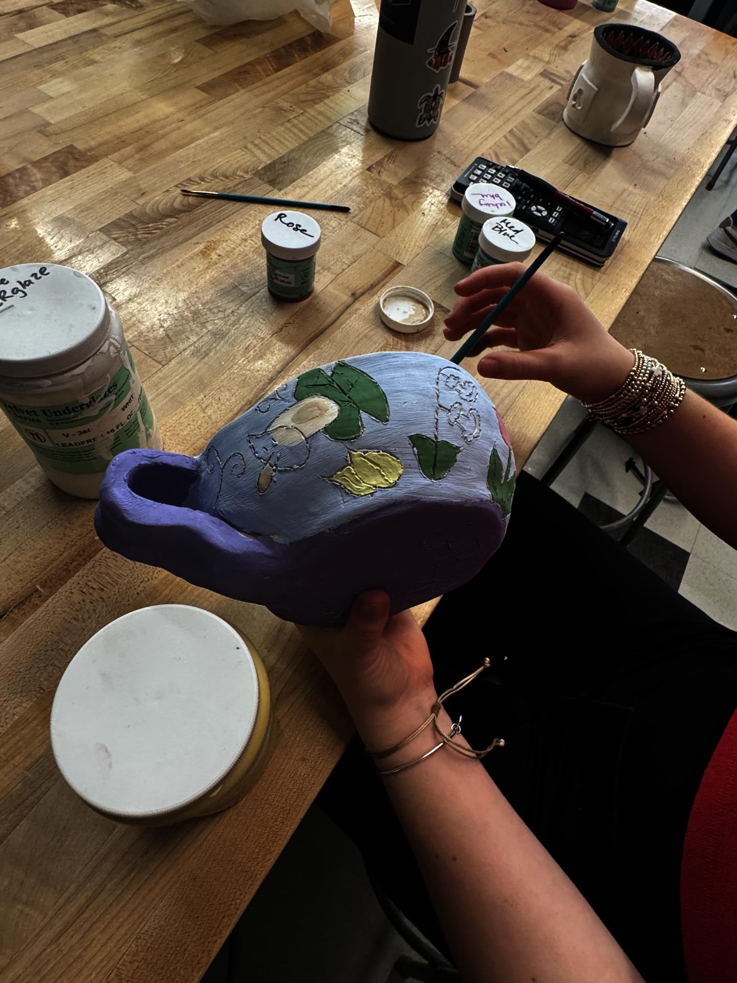 A student out of frame glazes an oversized tea cup with flowers on a blue and purple background