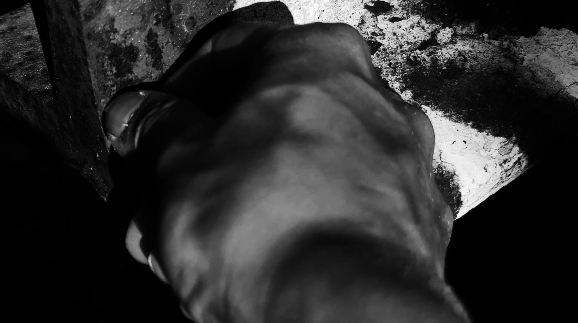 A close-up black and white shot with a hand scratching on the rusty metal surface with white graffiti.